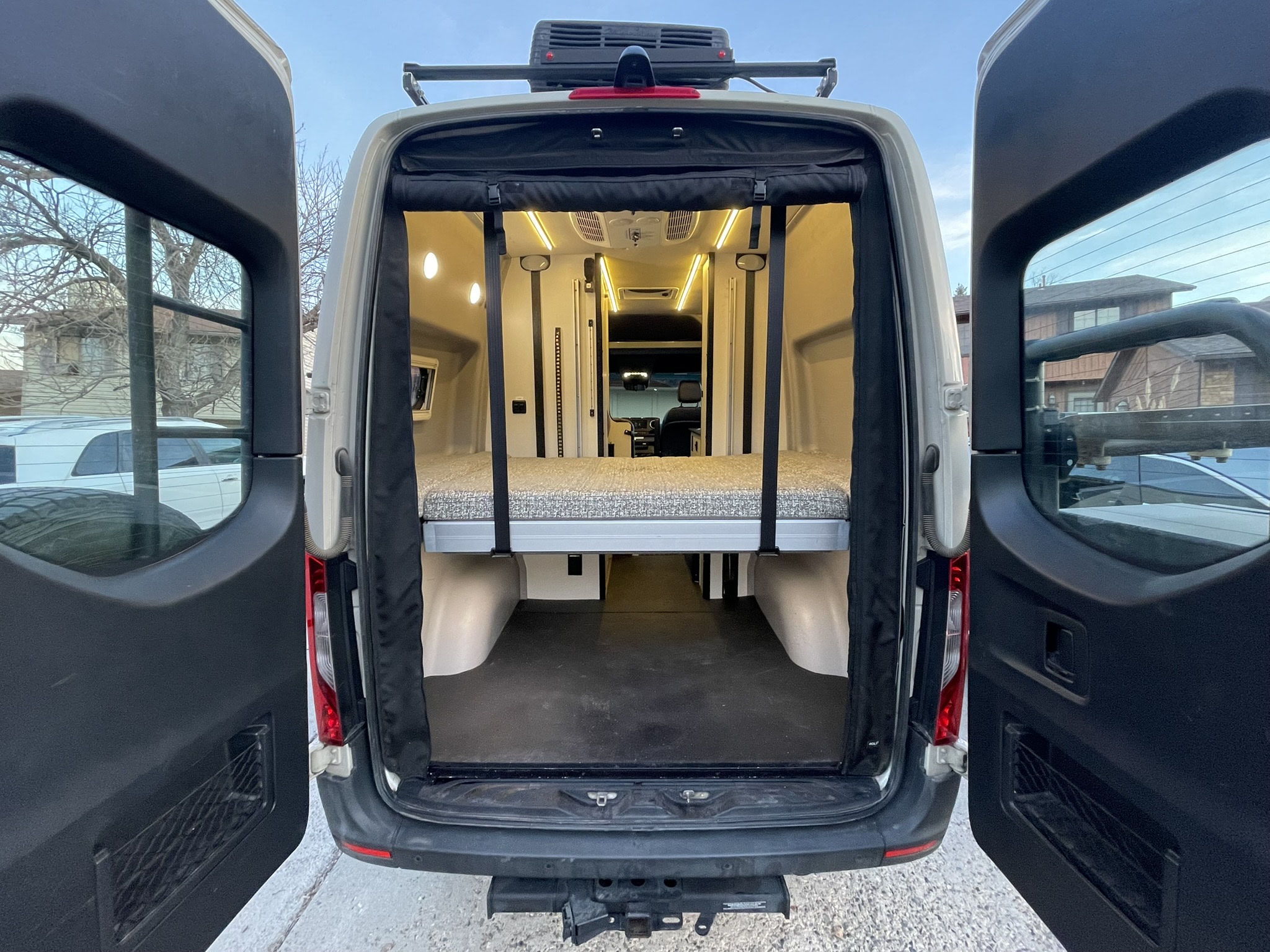 Rear interior of an RV rental camper van, showing an elevated bed, storage space, and bright LED lighting for van life.. Winnebago Revel 2020