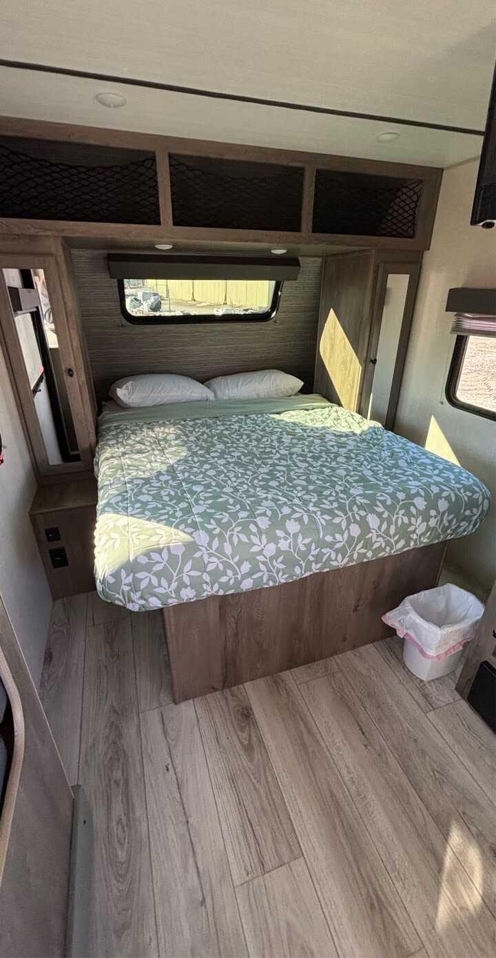 Cozy rv rental bedroom: green floral bed, overhead storage, window, and wood floor. Bright and inviting for your travels.. Forest River Surveyor 2022