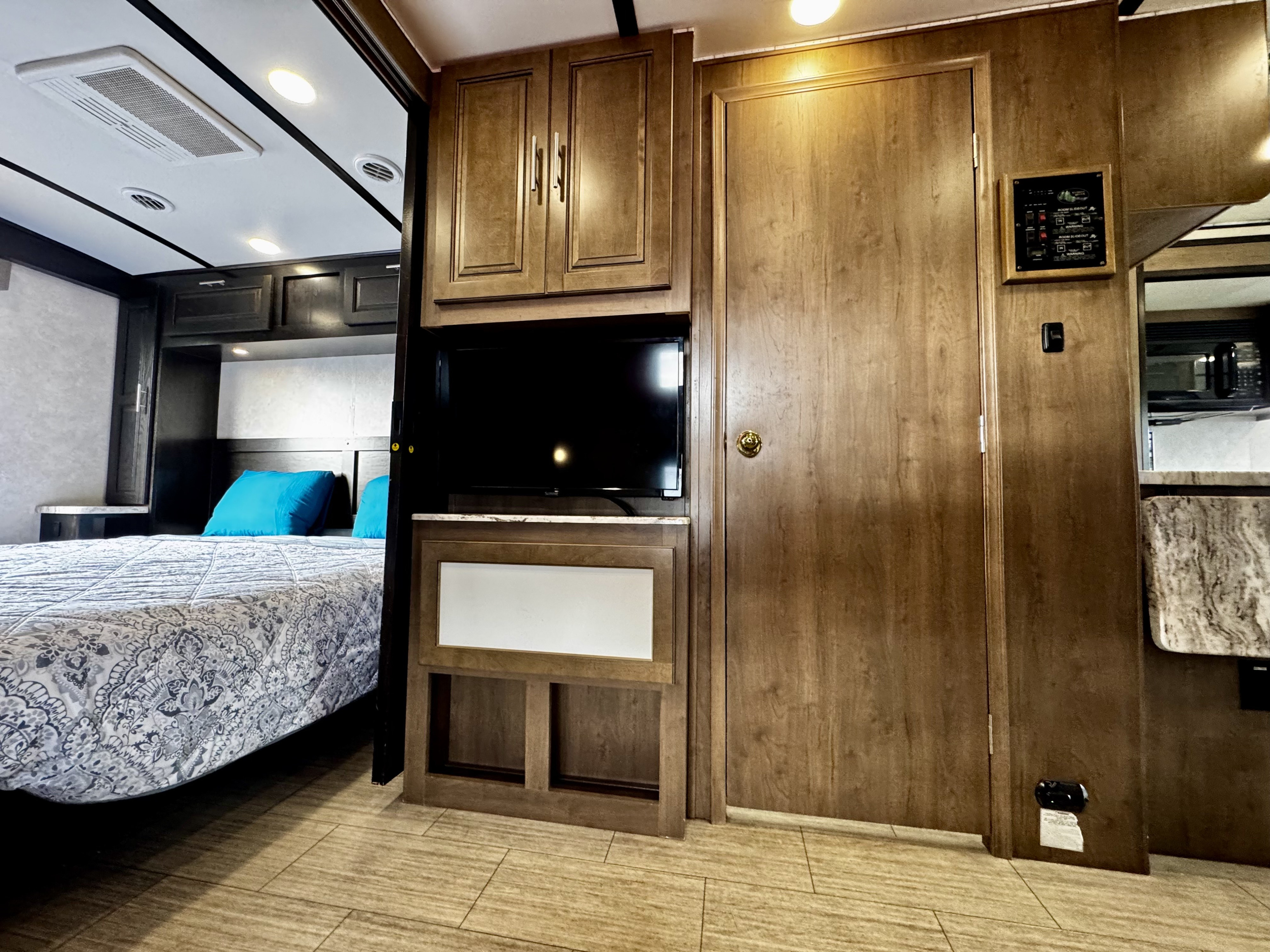 RV rental interior shows a comfortable bedroom, mounted TV, wood cabinetry, and a control panel for modern amenities.. Forest River FR3 2021