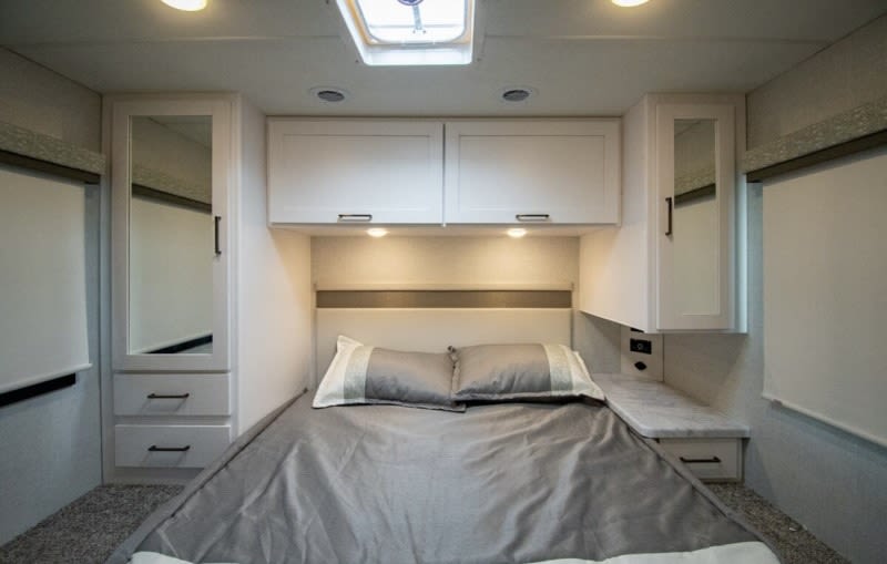 Bright RV rental bedroom with a comfy bed, overhead white cabinets, and mirrored storage. Perfect for your trip.. thor four winds 2026