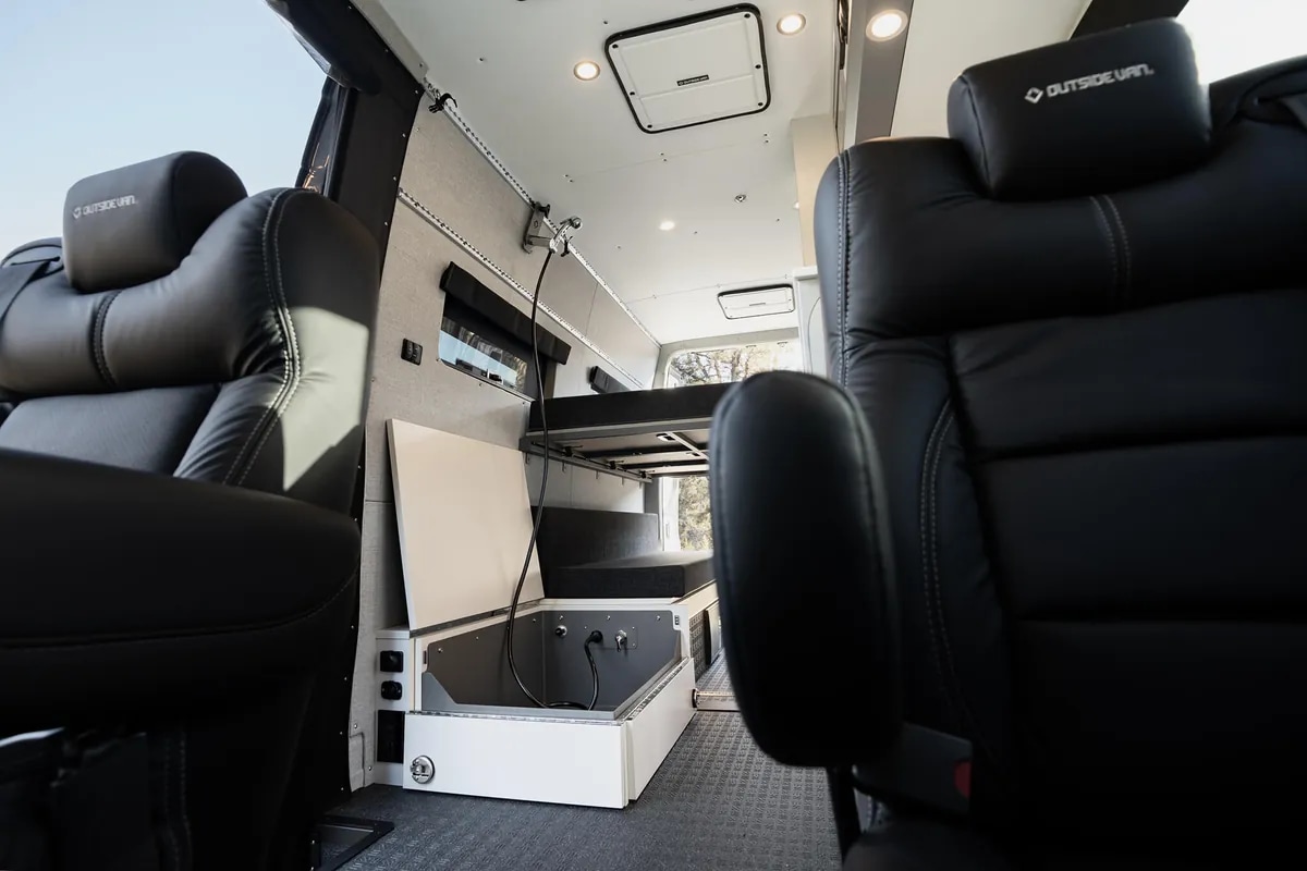 Inside a premium RV rental: Black leather seats face a versatile bed and storage with visible power outlets.. Outside Van Approach 170 2024