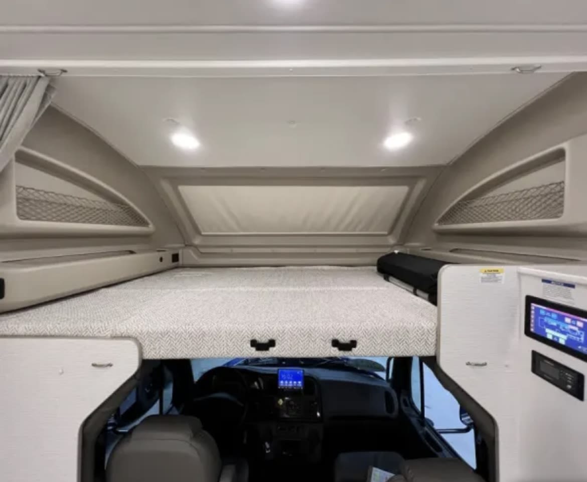 This RV rental interior features a cozy cab-over bed above the driver's area, with a visible dashboard and control panel.. Entegra Coach Accolade XL 2023