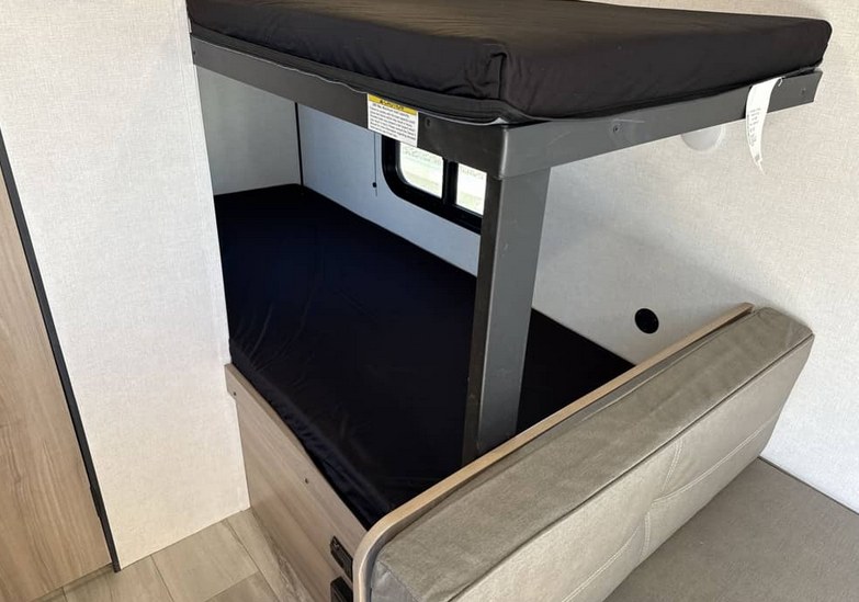 Inside this RV rental, discover comfy bunk beds with black mattresses and a nearby gray upholstered seating bench.. Keystone RV Coleman 2026