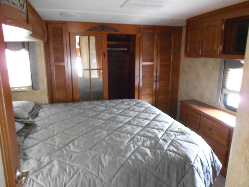 Spacious RV rental bedroom features a large bed with grey comforter, mirrored closet, wooden cabinets, and a window.. Keystone RV Alpine 2013