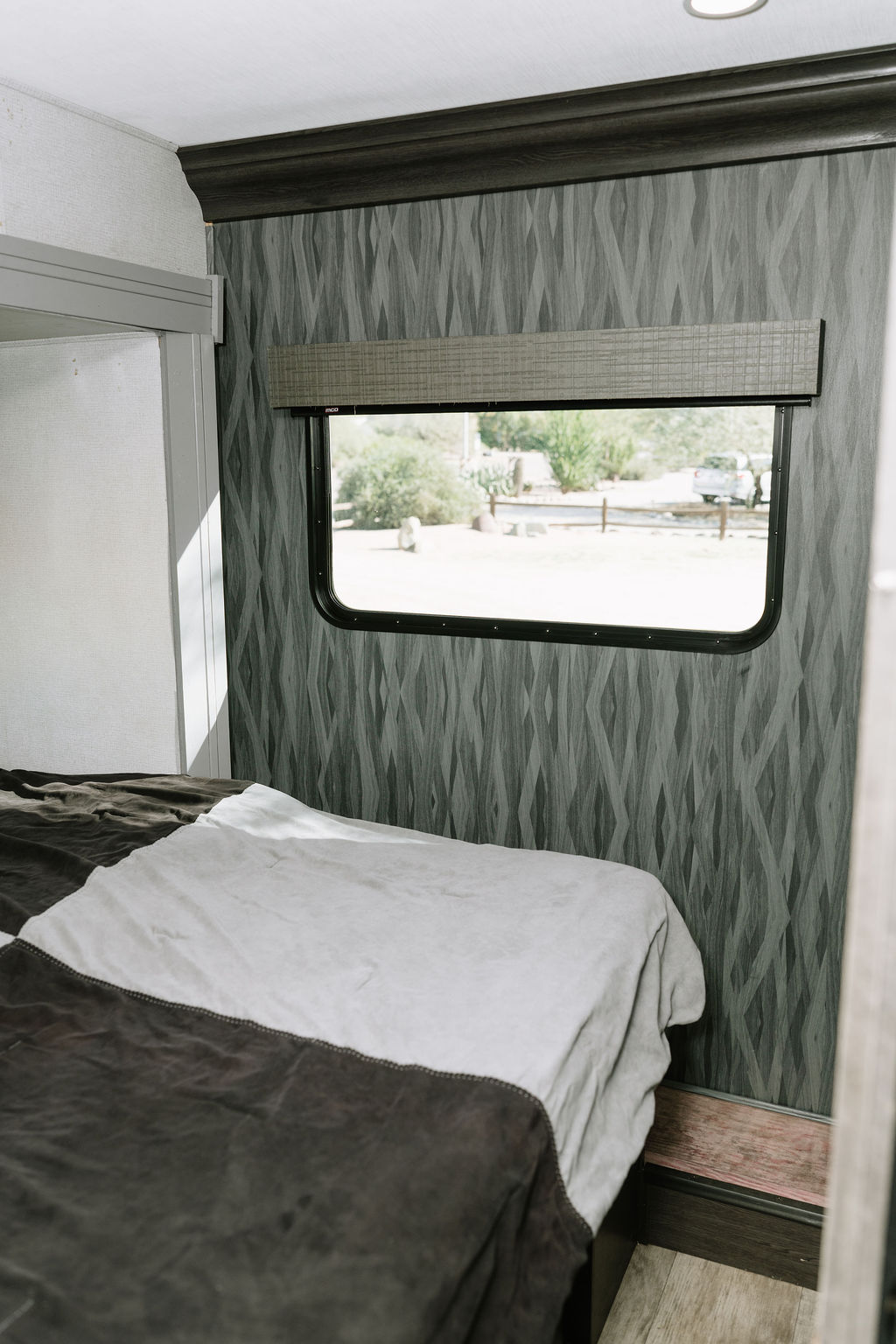 This RV rental bedroom features a comfy bed, a modern patterned wall, and a window view of the outdoors.. Forest River Solera 2022