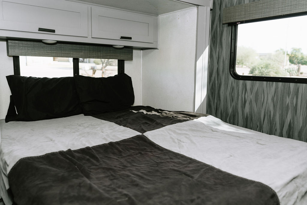 Explore a comfortable RV rental bedroom, featuring a checkered duvet, black pillows, white cabinets, and scenic window views.. Forest River Solera 2022