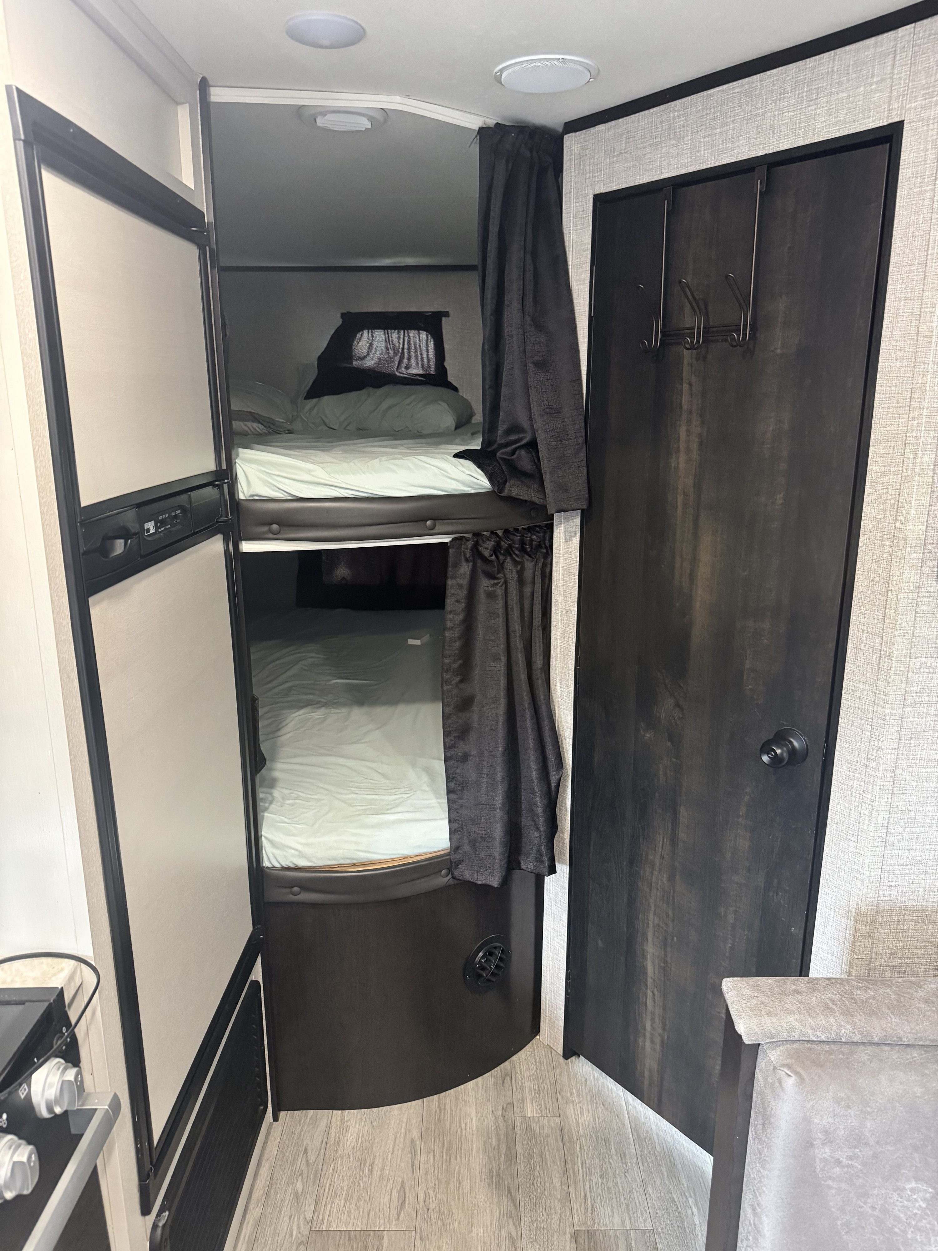 Cozy RV rental interior featuring bunk beds with curtains, a refrigerator, and a dark wood door with hooks, ideal for family travel.. Jayco Jay Flight SLX 2021