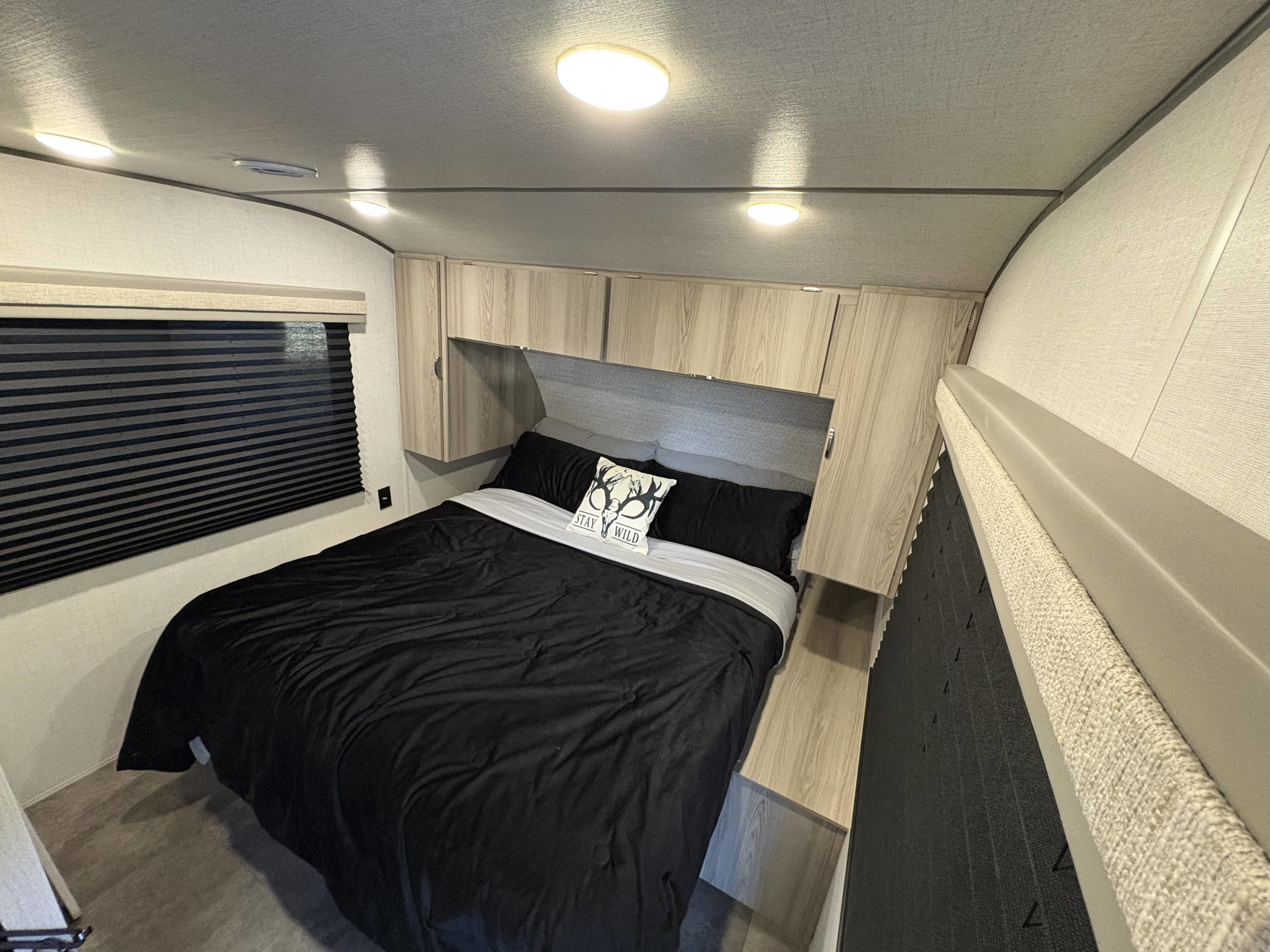 Comfortable RV rental bedroom featuring black bedding, wood cabinets, a window with blinds, and bright ceiling lights.. Forest River Salem FSX 2025