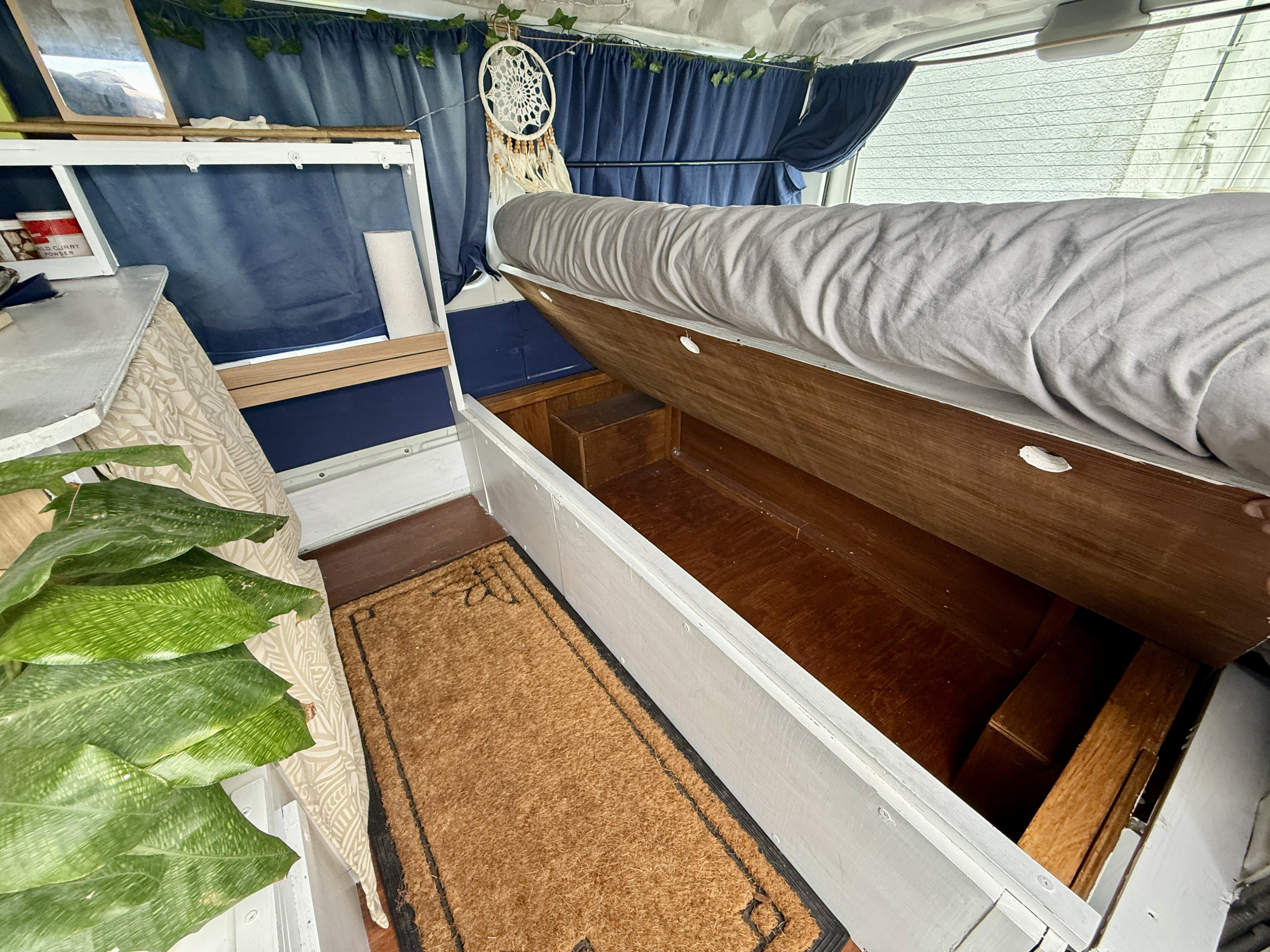 Cozy RV rental interior with a lifted bed displaying smart under-bed storage, perfect for compact travel adventures.. Mazda Bongo, Gekko conversion 2004