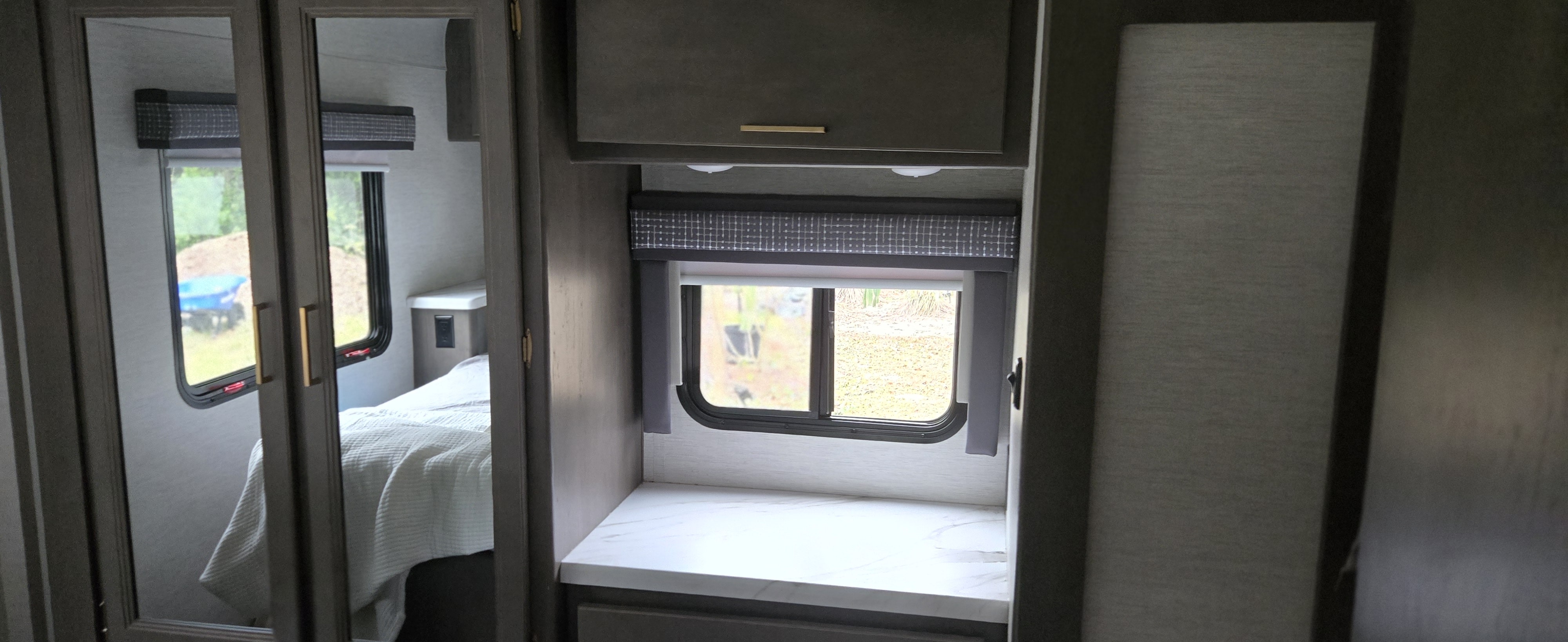 Modern RV rental interior: bedroom reflected in mirrored closet doors, adjacent to a window with a countertop.. Thor Chateau 2024