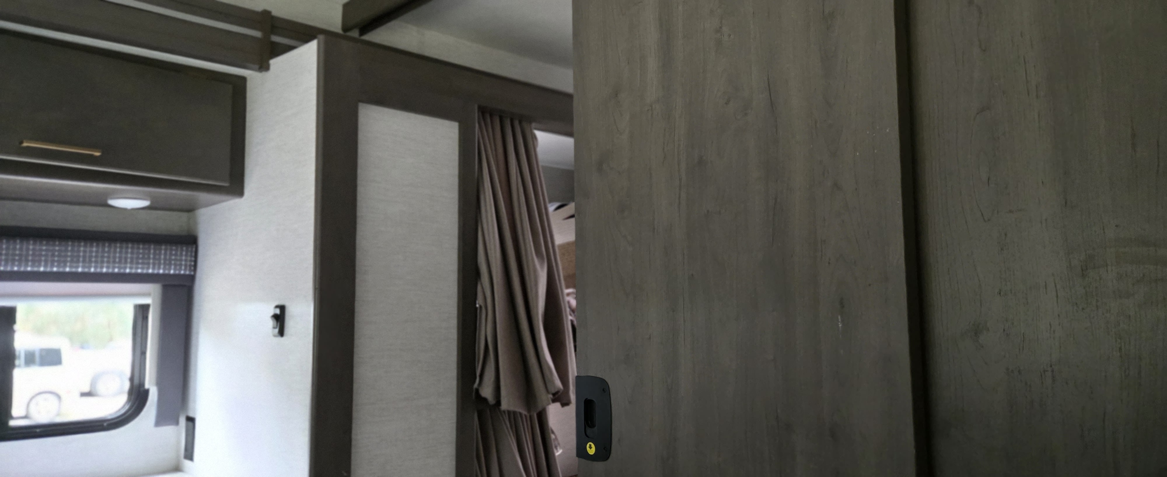 RV rental interior with wood cabinets, a window, and a partially open doorway featuring a curtain and sliding door.. Thor Chateau 2024
