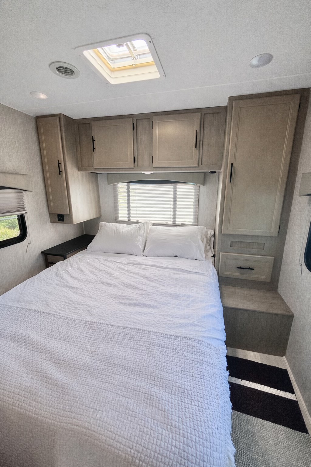Cozy RV rental bedroom featuring a comfy bed with white linens, overhead cabinets, and a ceiling skylight.. Forest River Coachmen Freelander 2022