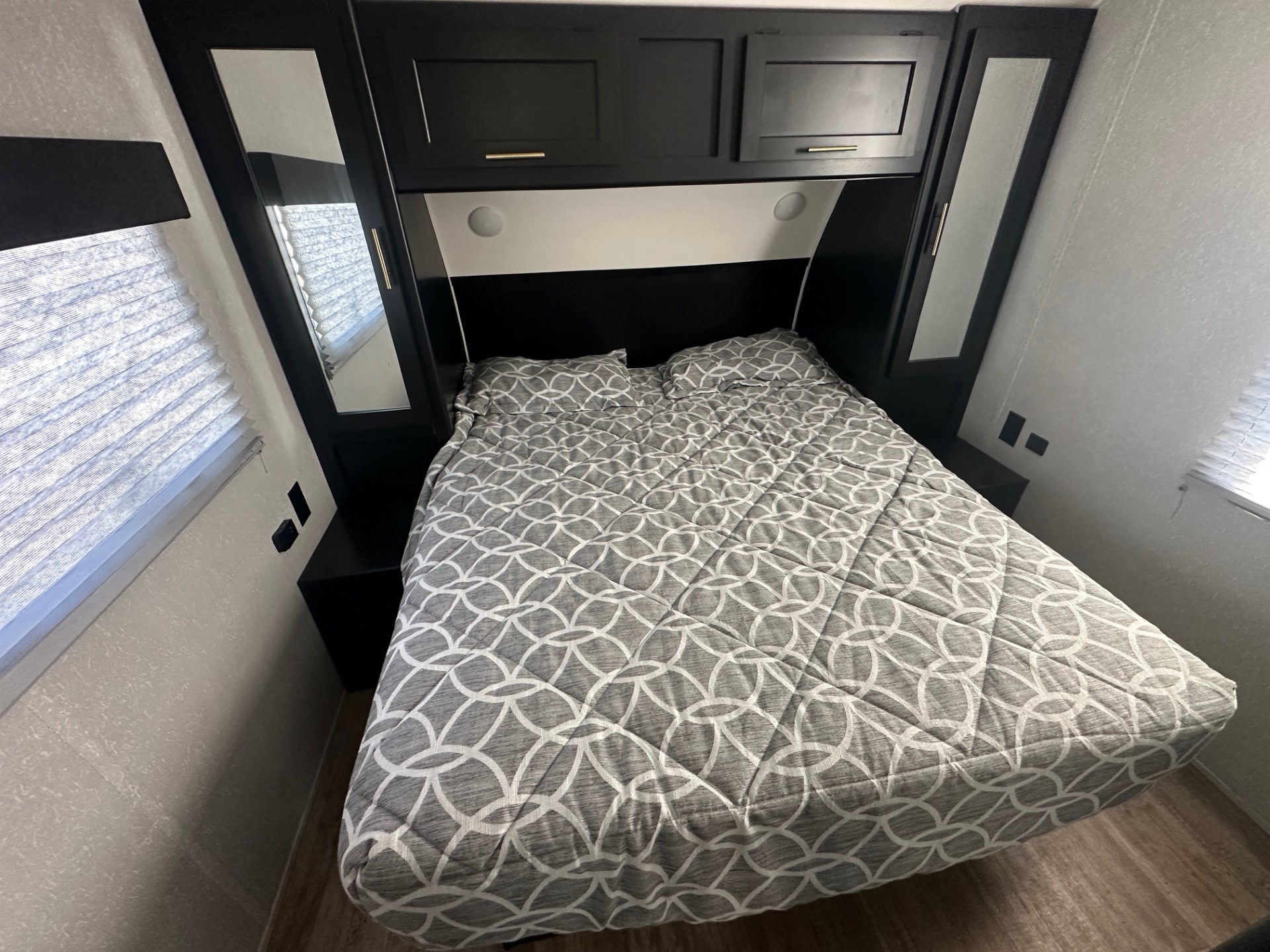 Modern RV rental bedroom featuring dark cabinetry, mirrored closets, a cozy patterned bed, and overhead storage.. Forest River Cherokee Grey Wolf 2022