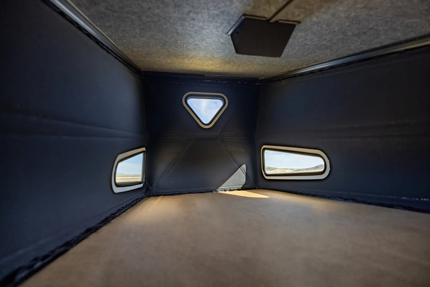 Inside an RV rental's compact sleeping area: dark walls, light ceiling, and floor, with windows viewing a desert.. Mercedes-Benz Sprinter 2026
