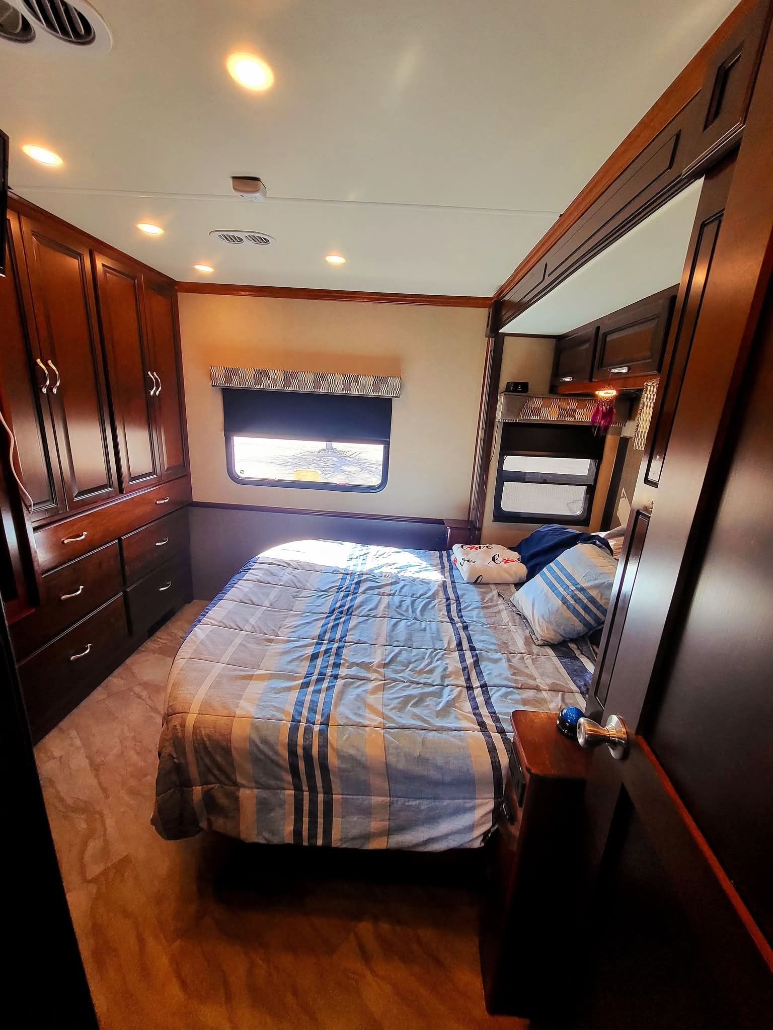 Interior of a spacious RV rental bedroom with a comfortable bed, dark wood cabinets, and a window to enjoy the journey.. Fleetwood Bounder 2017