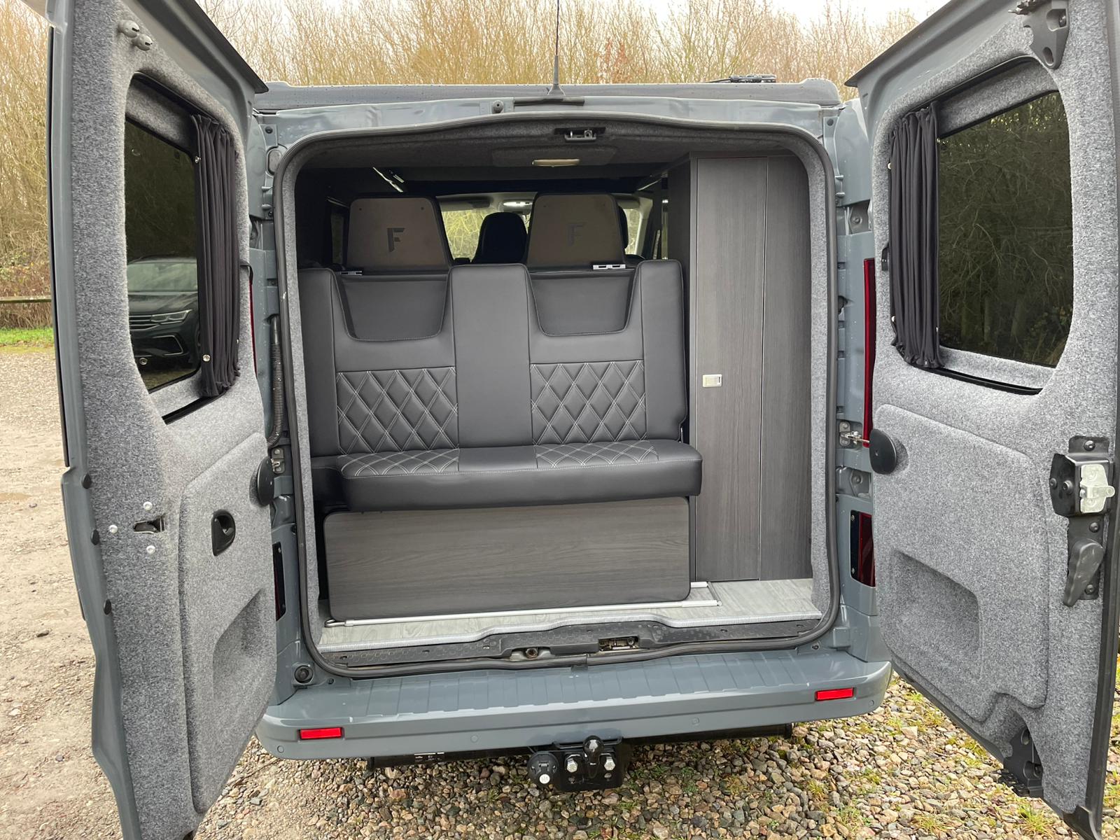 RV rental campervan's rear interior: comfy black seating, dark wood cabinet, grey carpet lining, and privacy curtains.. Renault Traffic 2020