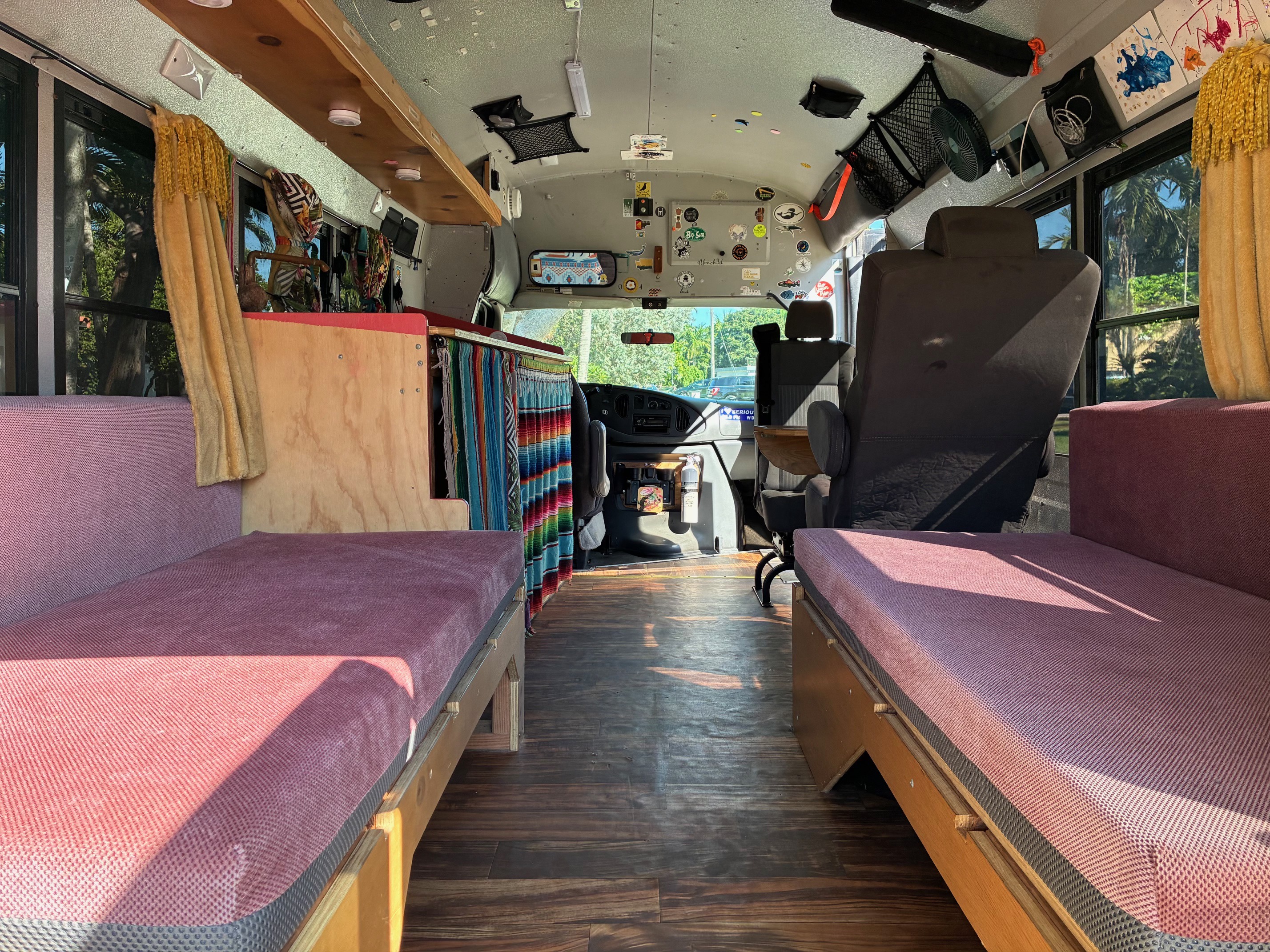 Cozy RV rental interior: Custom bus conversion with dual benches, wooden floor, and a view into the driver's cockpit.. Ford E350 Box Van 2004