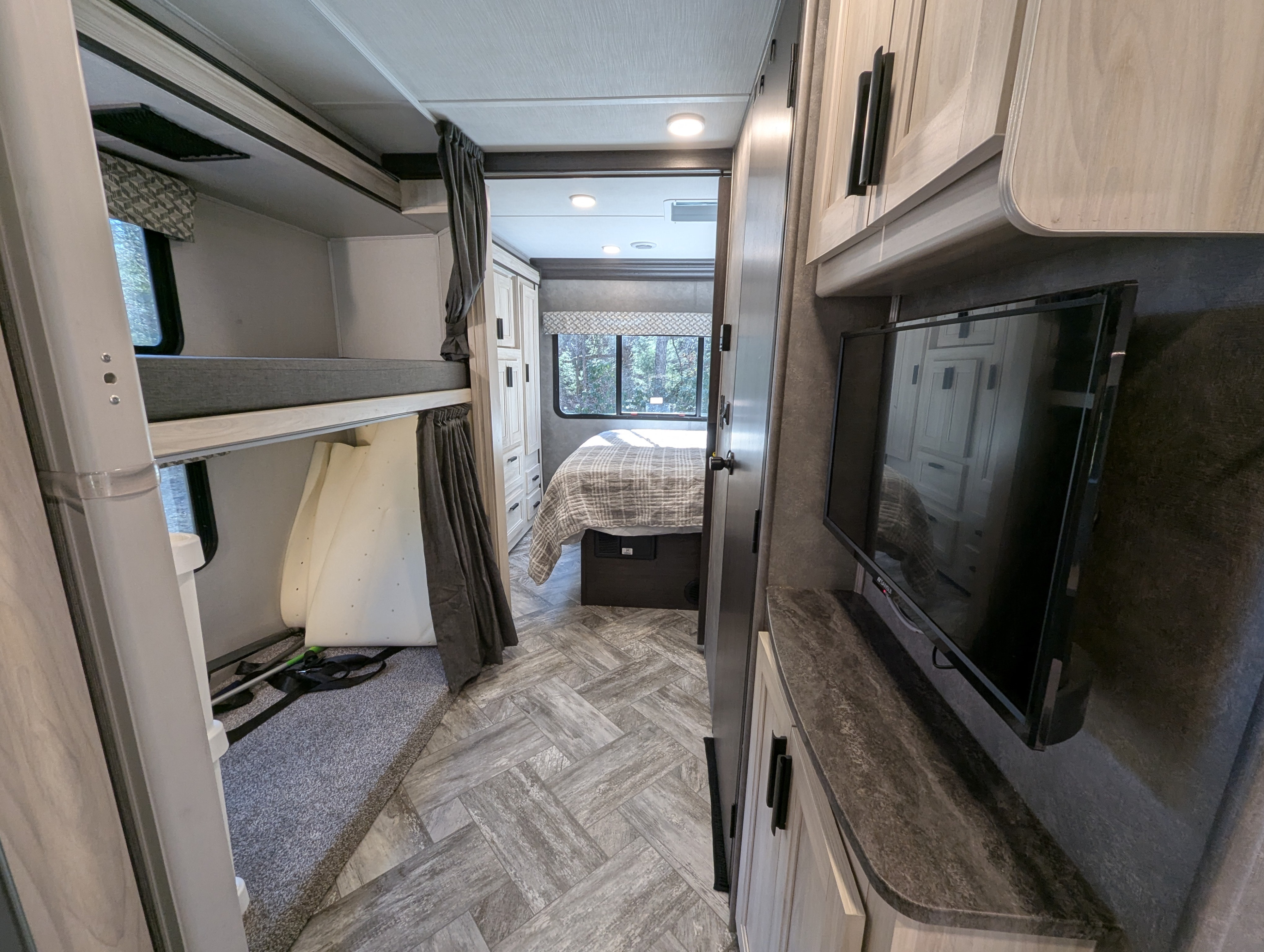 This RV rental interior features practical bunk beds on the left, a main bedroom straight ahead, and a TV area on the right.. Forest River Forester 2023