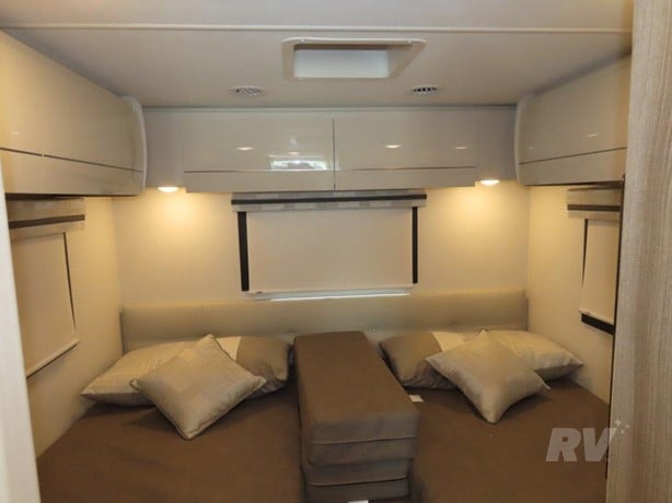 Modern **RV rental** interior: A bright **bedroom** with two **beds**, stylish pillows, and sleek overhead **cabinets** for storage.. Thor Axis 2024