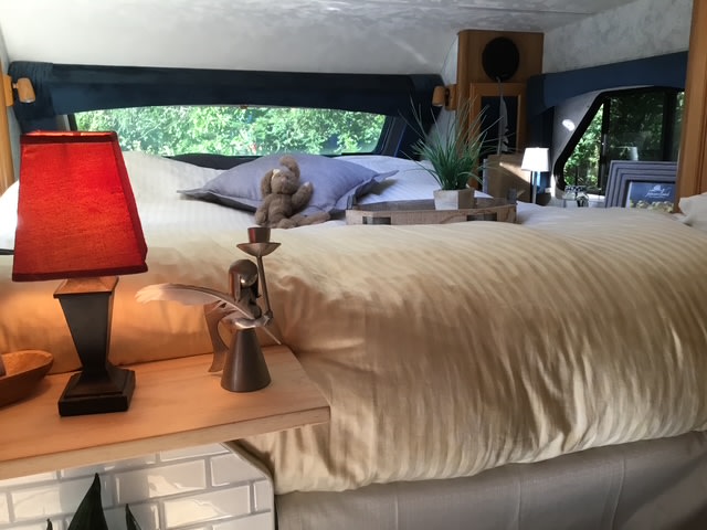 Cozy RV rental bedroom with a comfy bed, red lamp, and nature views from the windows, perfect for relaxation.. Ford Lance 2021