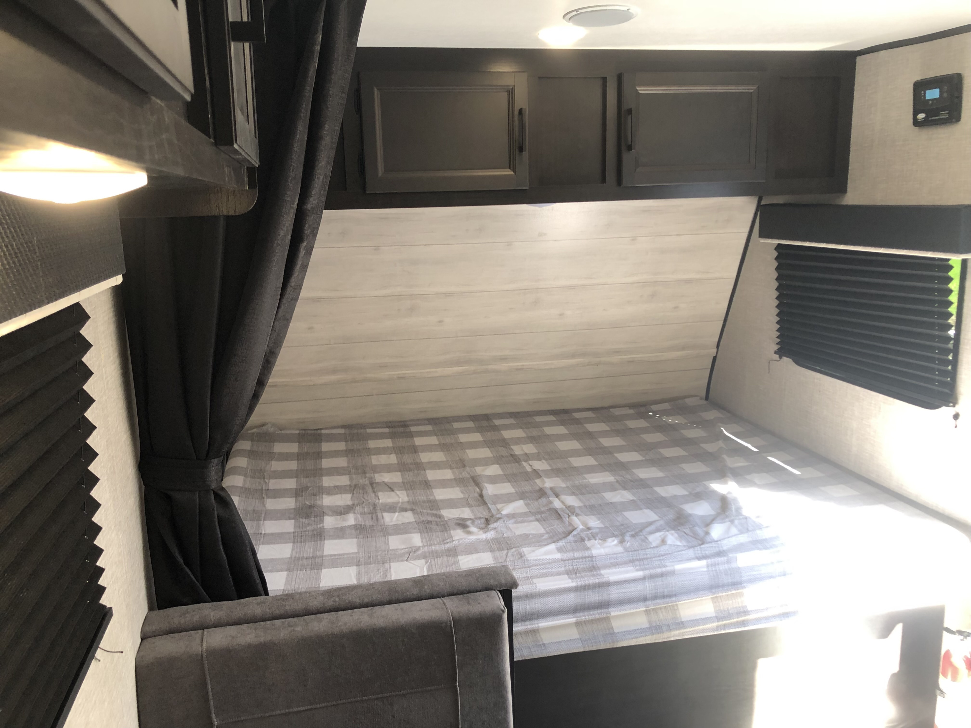 Cozy RV rental interior featuring a comfortable bed with plaid bedding, dark overhead cabinets, and built-in seating.. Jayco Jay Flight SLX 2022
