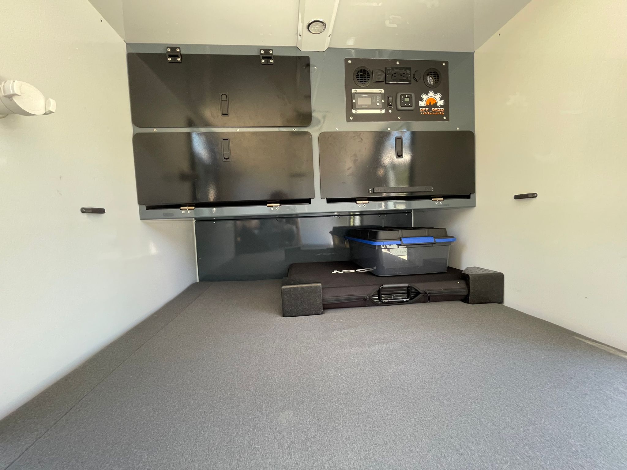 This RV rental interior offers organized storage compartments, a utility control panel, and a carpeted floor, perfect for off-grid travel.. Off Grid Trailers Off Grid Trailers Trailer 2021