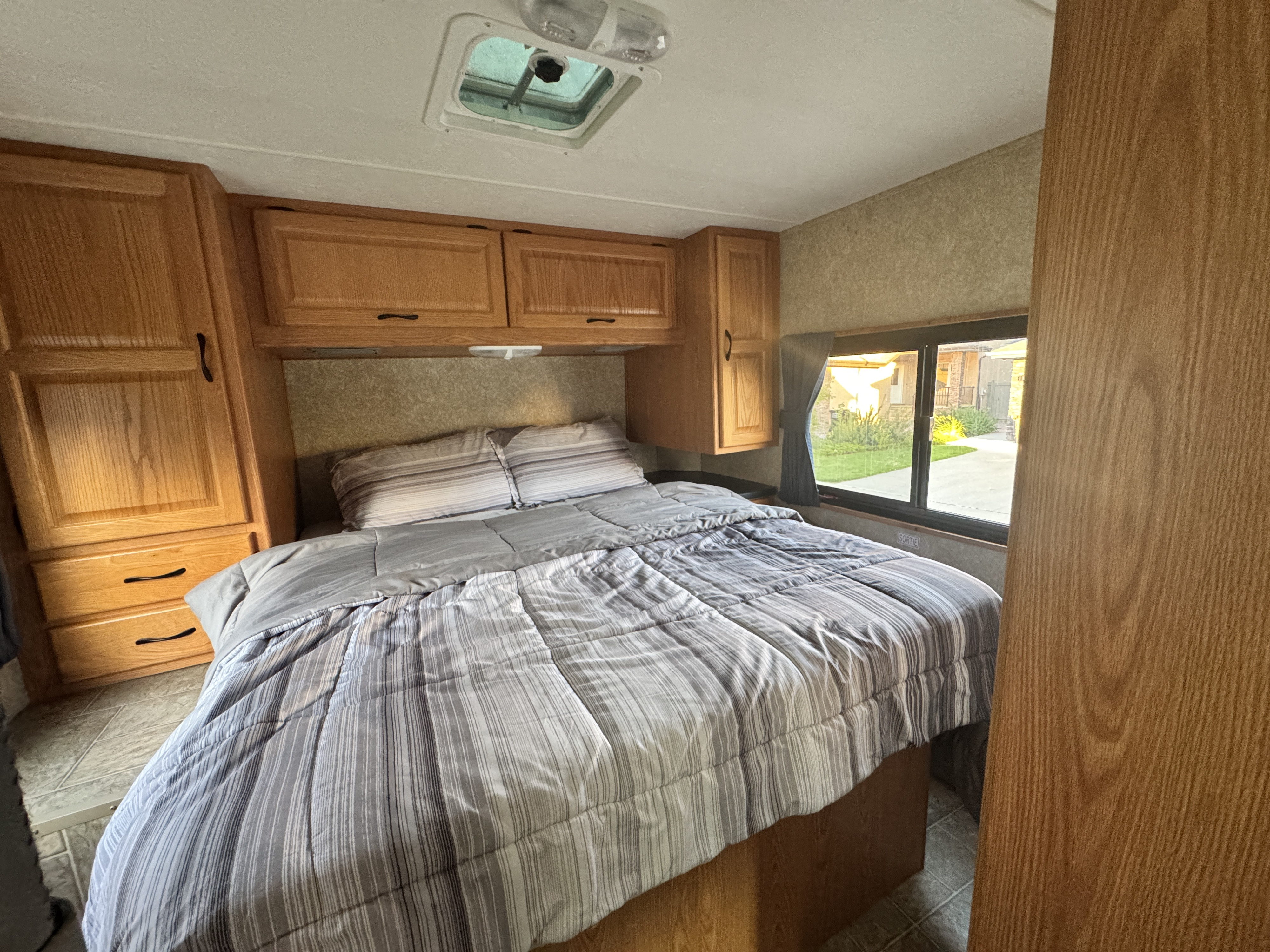 Cozy RV rental bedroom features a comfortable bed with striped linens, wood cabinets, and an overhead vent, perfect for travel.. Four Winds Majestic 2011