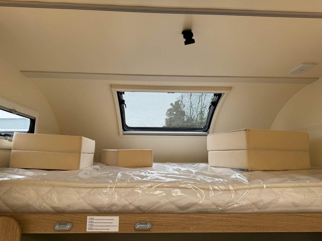 RV rental interior: A bed with plastic-wrapped mattress & cream cushions sits under curved ceilings & windows, ready for adventure.. Auto Roller 746 Roller Team 746 2025