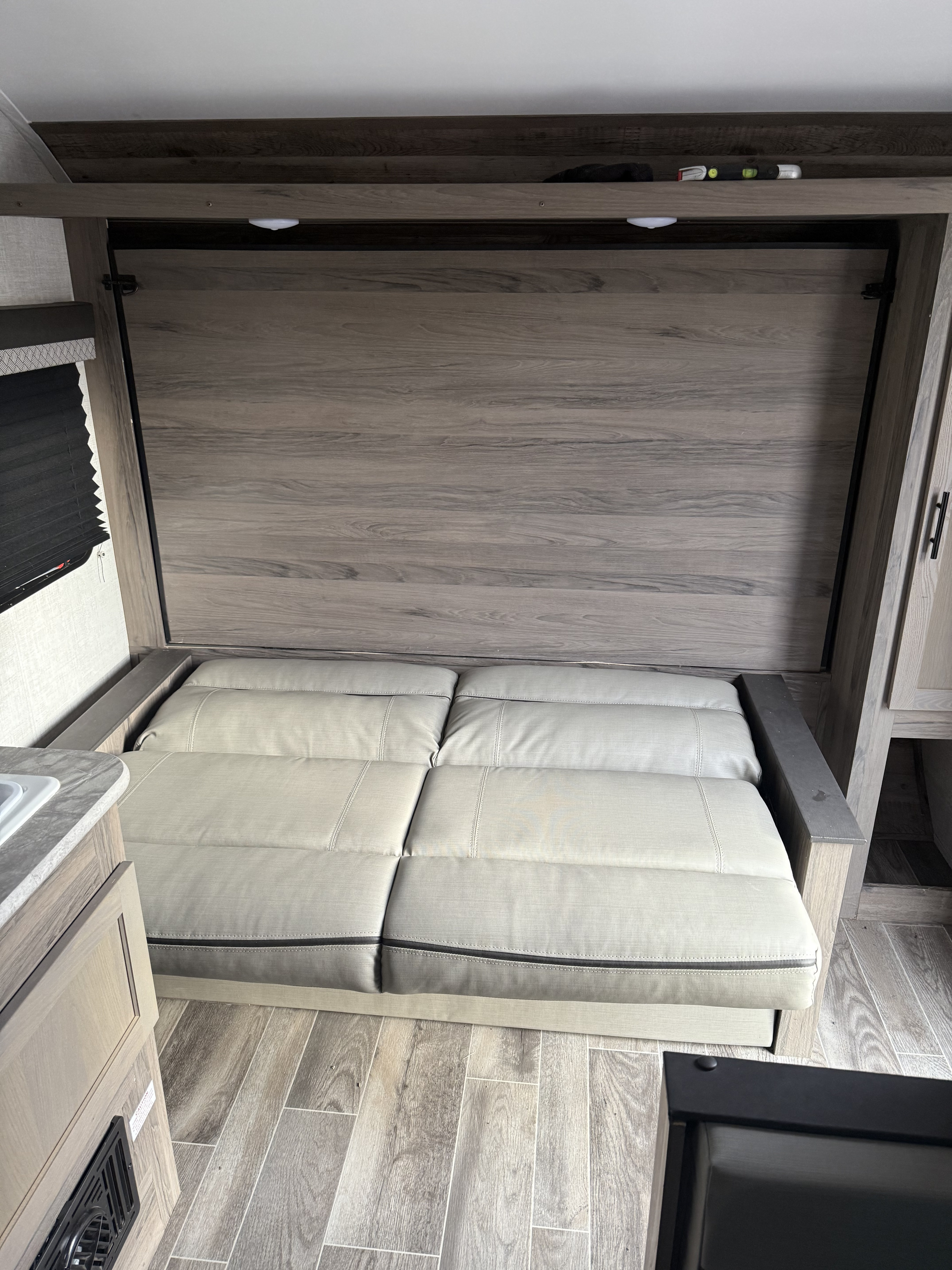 RV rental interior featuring a light gray convertible sofa bed, wood-look walls, and flooring in a compact living area.. Gulf Stream Ameri-Lite Super Lite 2023