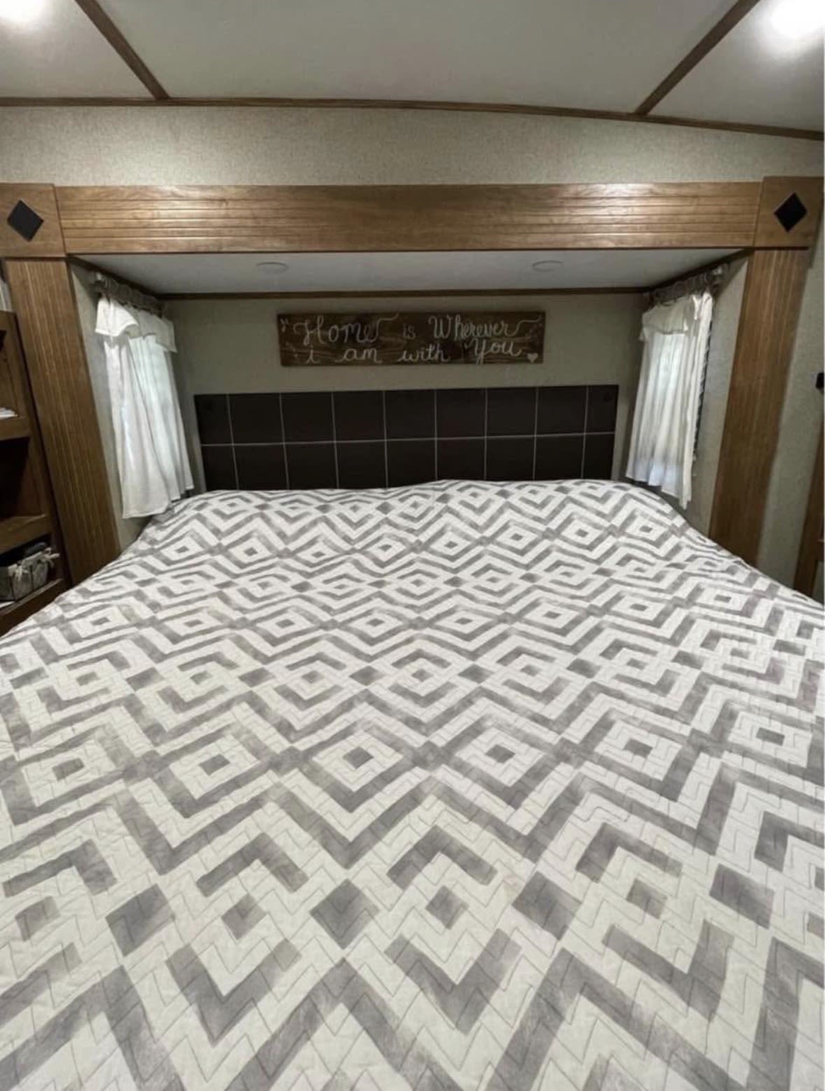 RV rental bedroom with a bed, geometric quilt, and "Home is Wherever I am with You" sign above the headboard.. Keystone RV Laredo 2019