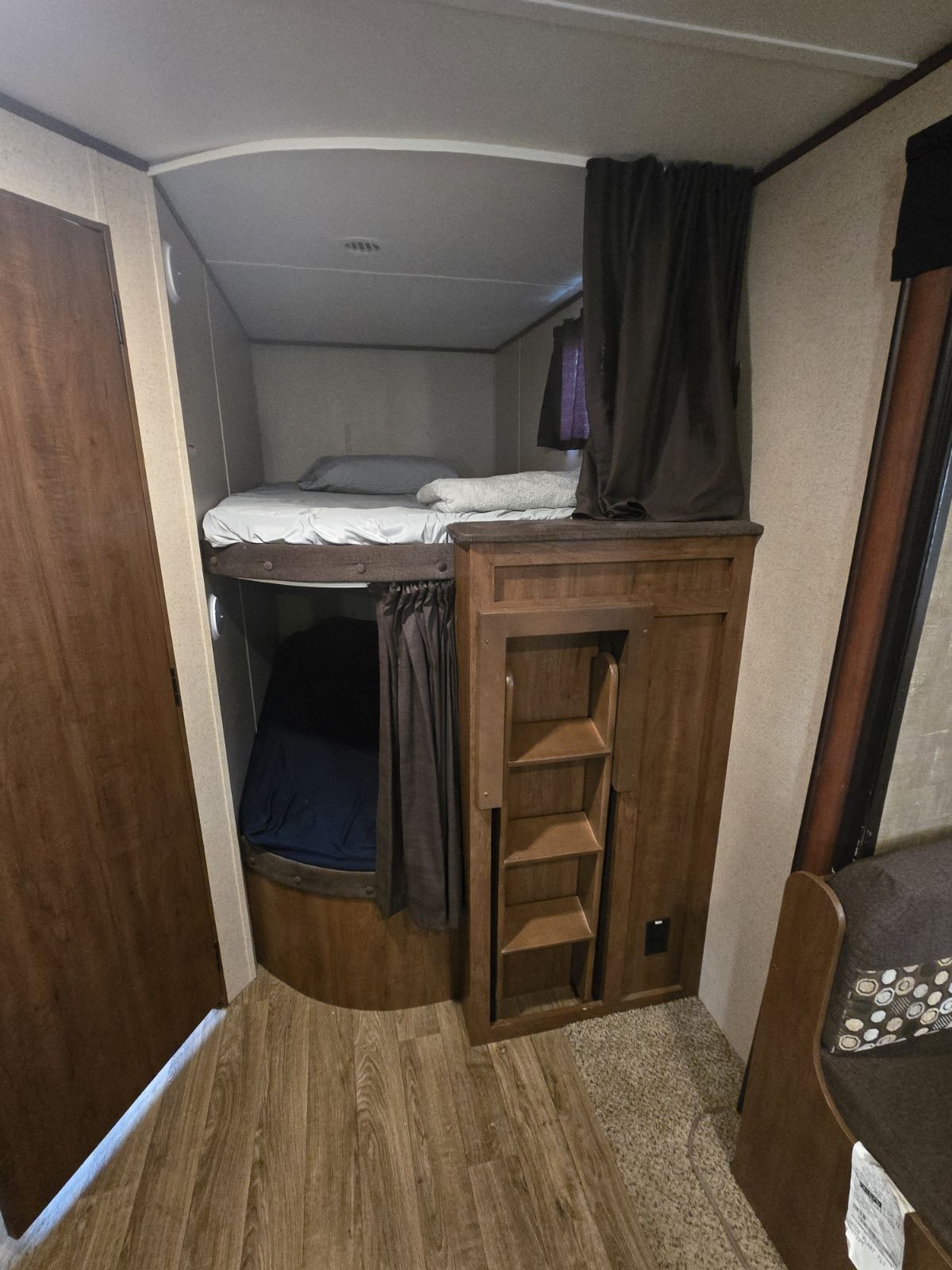 Inside an RV rental, a bunk bed area with two cozy beds, privacy curtains, and a wooden fold-down ladder.. Jay Flight SLX 287BHSW 2016