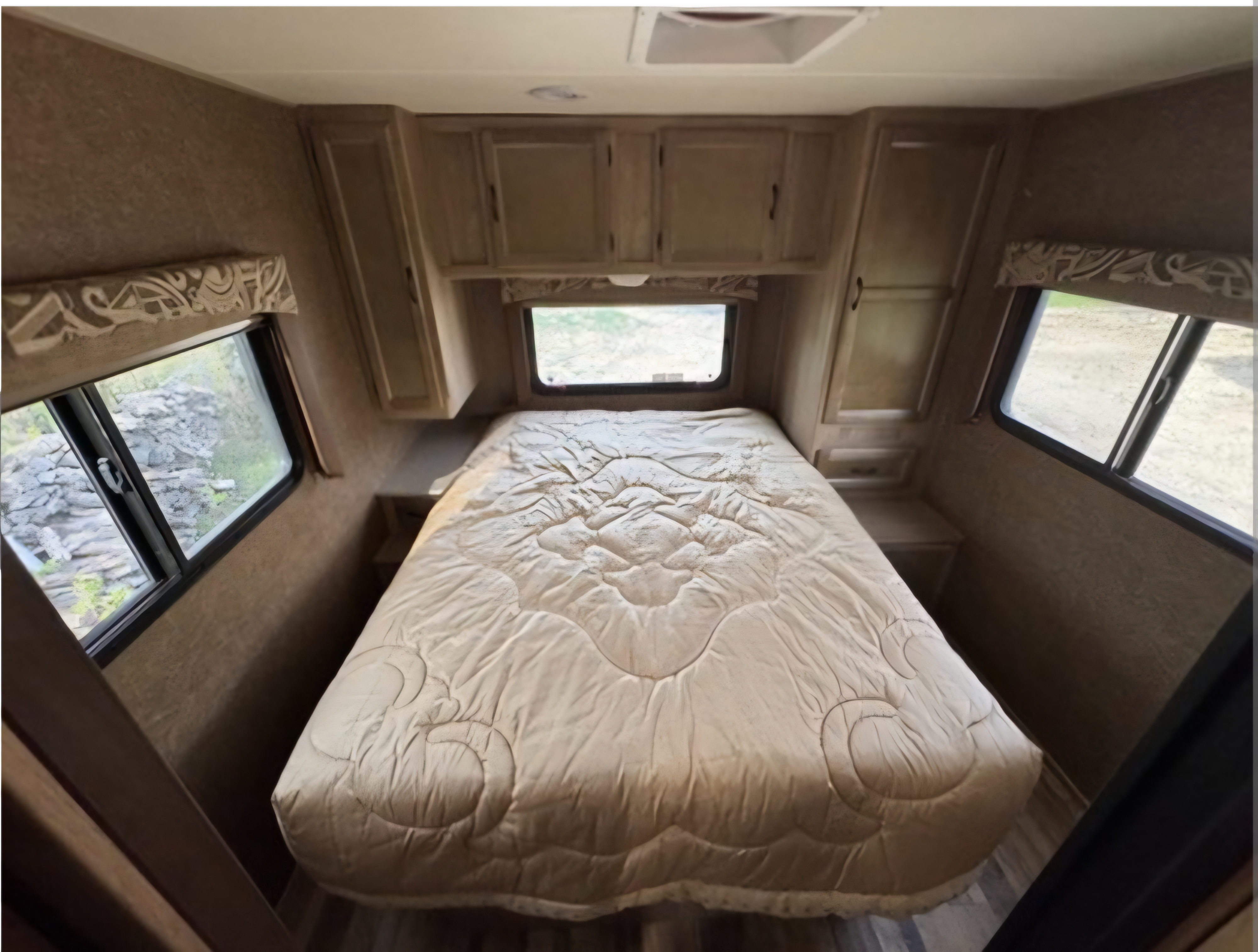 Cozy RV rental bedroom features a quilted bed, overhead cabinets, and windows, offering a compact, functional interior.. Coach House Coachman 2015