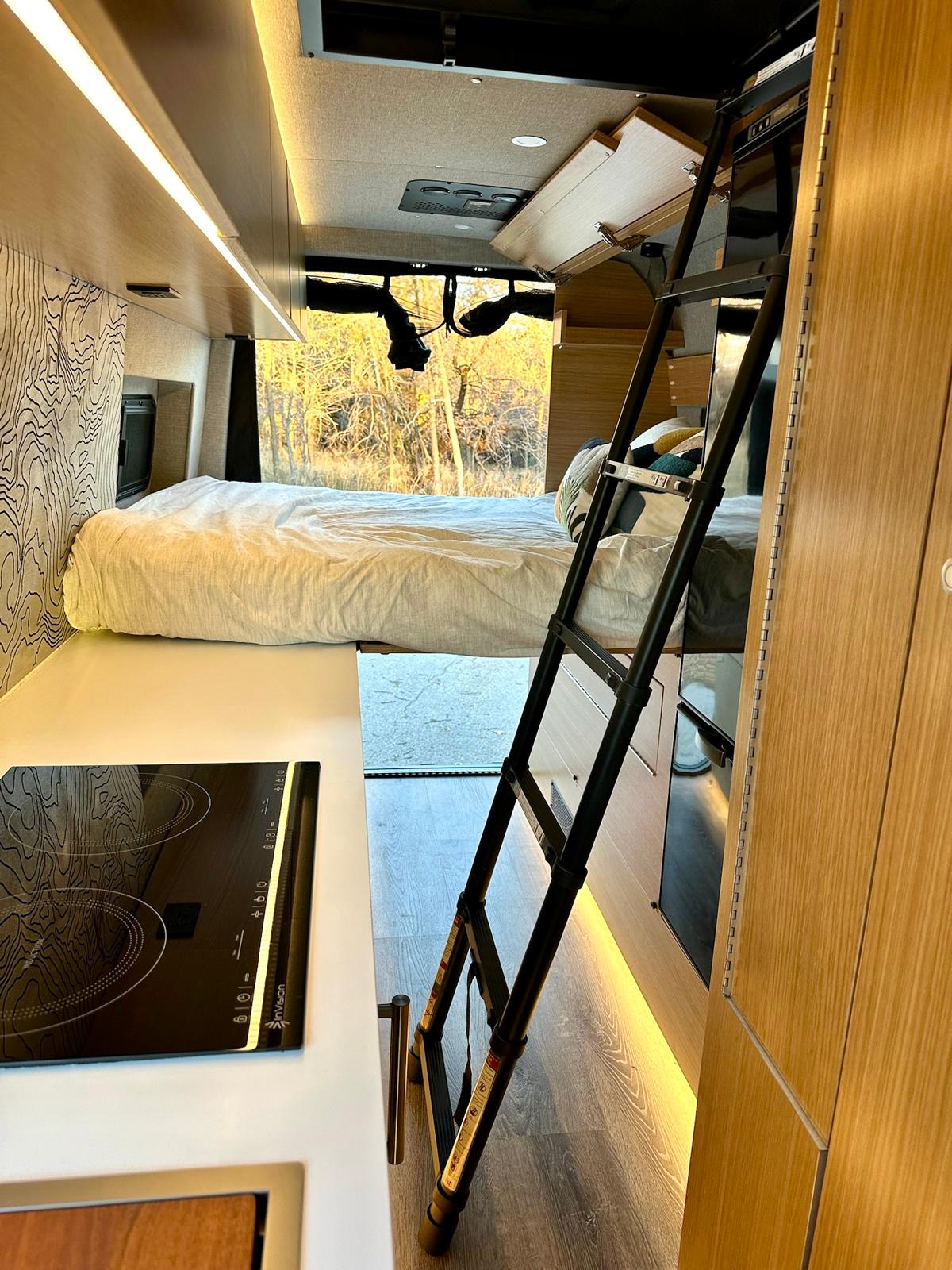 Explore this modern rv rental: a cozy interior with a bed, kitchen cooktop, and ladder to a loft, overlooking scenic nature.. Rossmonster Skye 2025