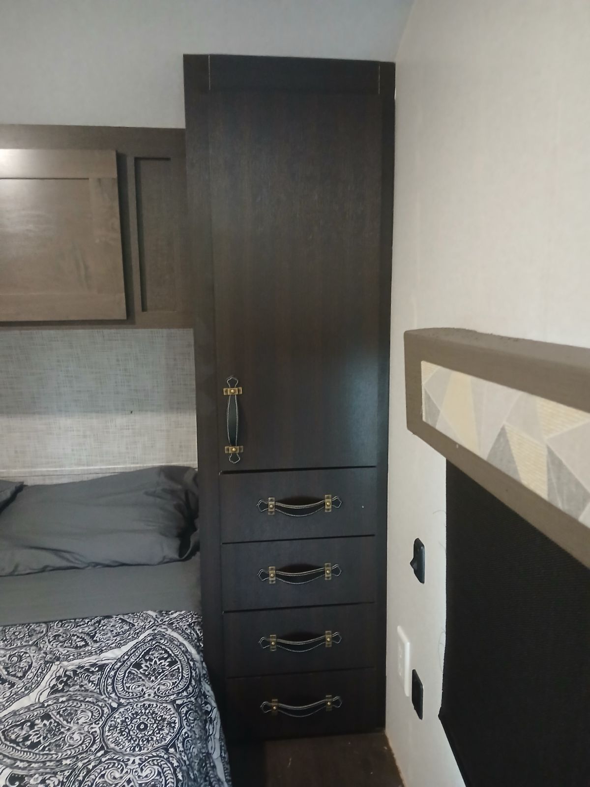 Cozy rv rental bedroom showing a tall wardrobe with drawers, a bed with patterned bedding, and overhead cabinets.. Salem 32BHDS 2020