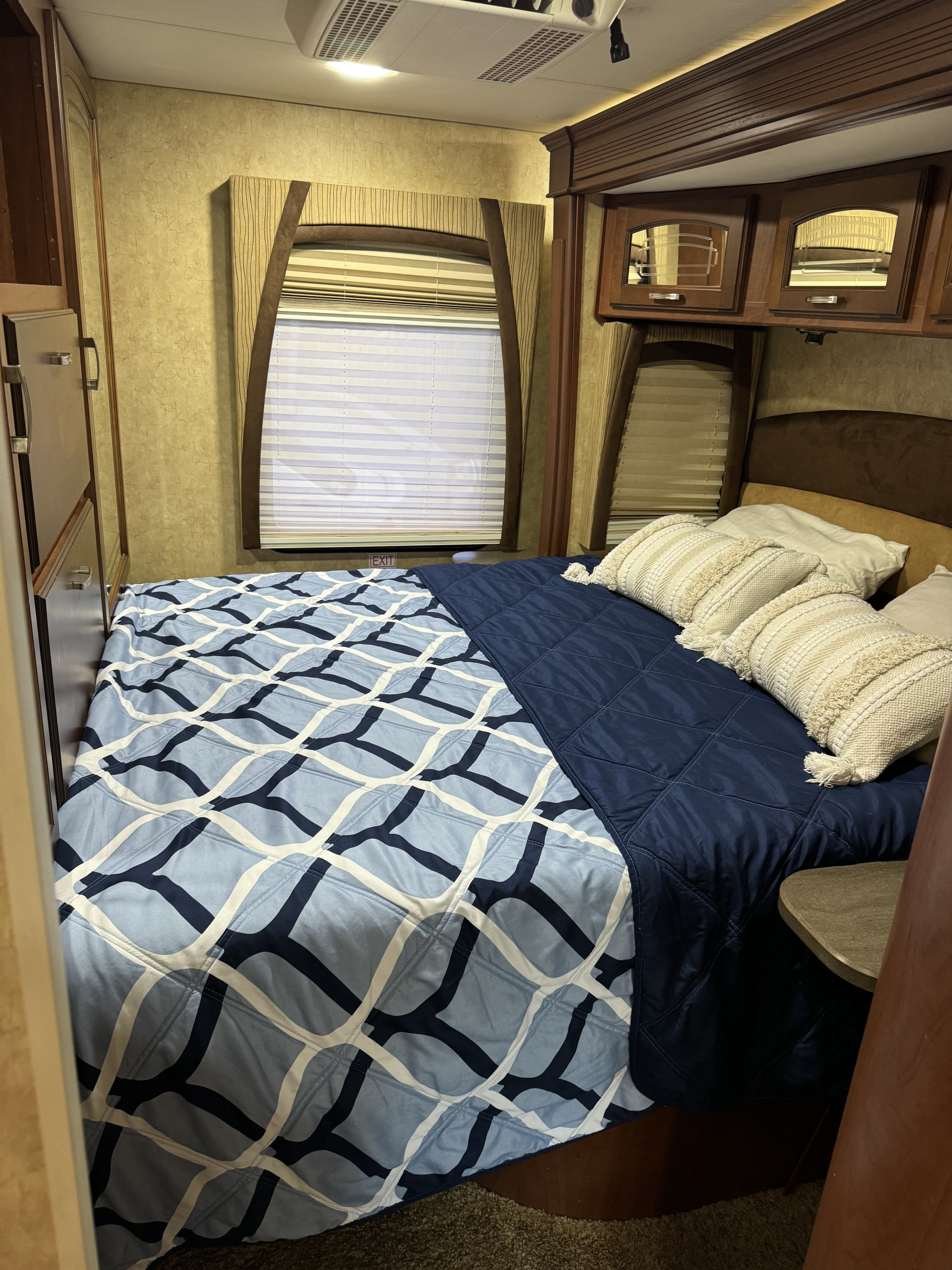 Cozy RV rental bedroom with a comfy bed, patterned bedding, overhead cabinets, and windows with blinds. Perfect for your next trip!. Jayco Melbourne 2012