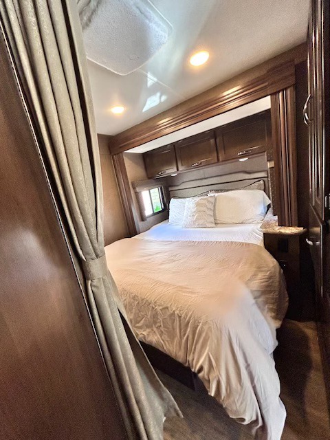Cozy RV rental bedroom featuring a large bed, wood accents, and ambient lighting, offering a private space for travel.. Thor Freedom Elite 2019