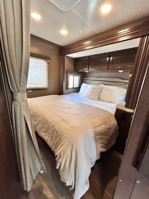 Comfortable RV rental bedroom with a large bed, dark wood cabinetry, and ambient lighting, offering a relaxing retreat.. Thor Freedom Elite 2019