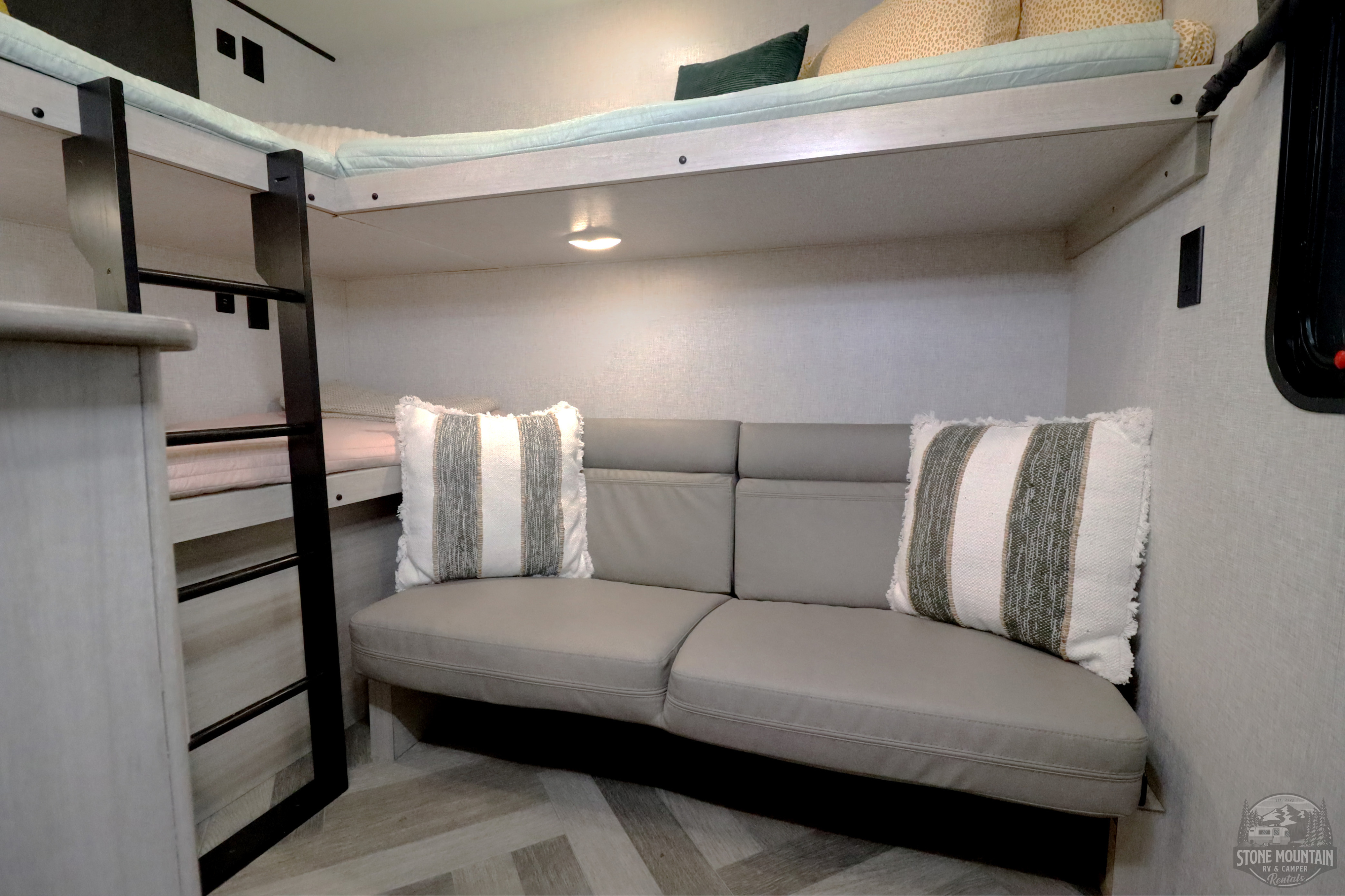 Cozy RV rental interior showcasing bunk beds, a ladder, and a comfy sofa with decorative pillows for relaxing.. Crossroads RV Zinger 2024