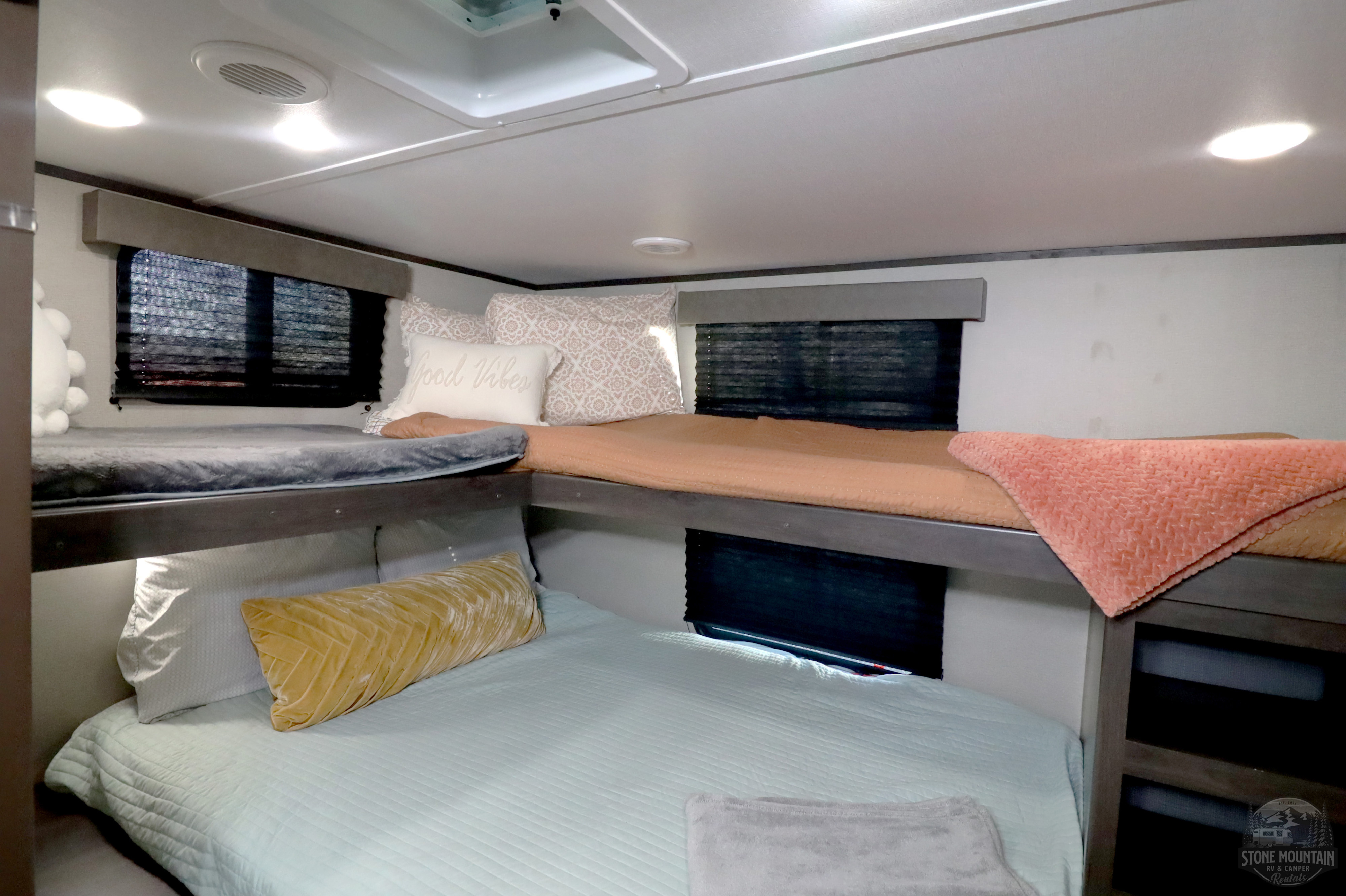 Inside this RV rental, comfortable bunk beds with vibrant blankets and pillows create a cozy camper sleeping area.. Grand Design Transcend Xplor 2023