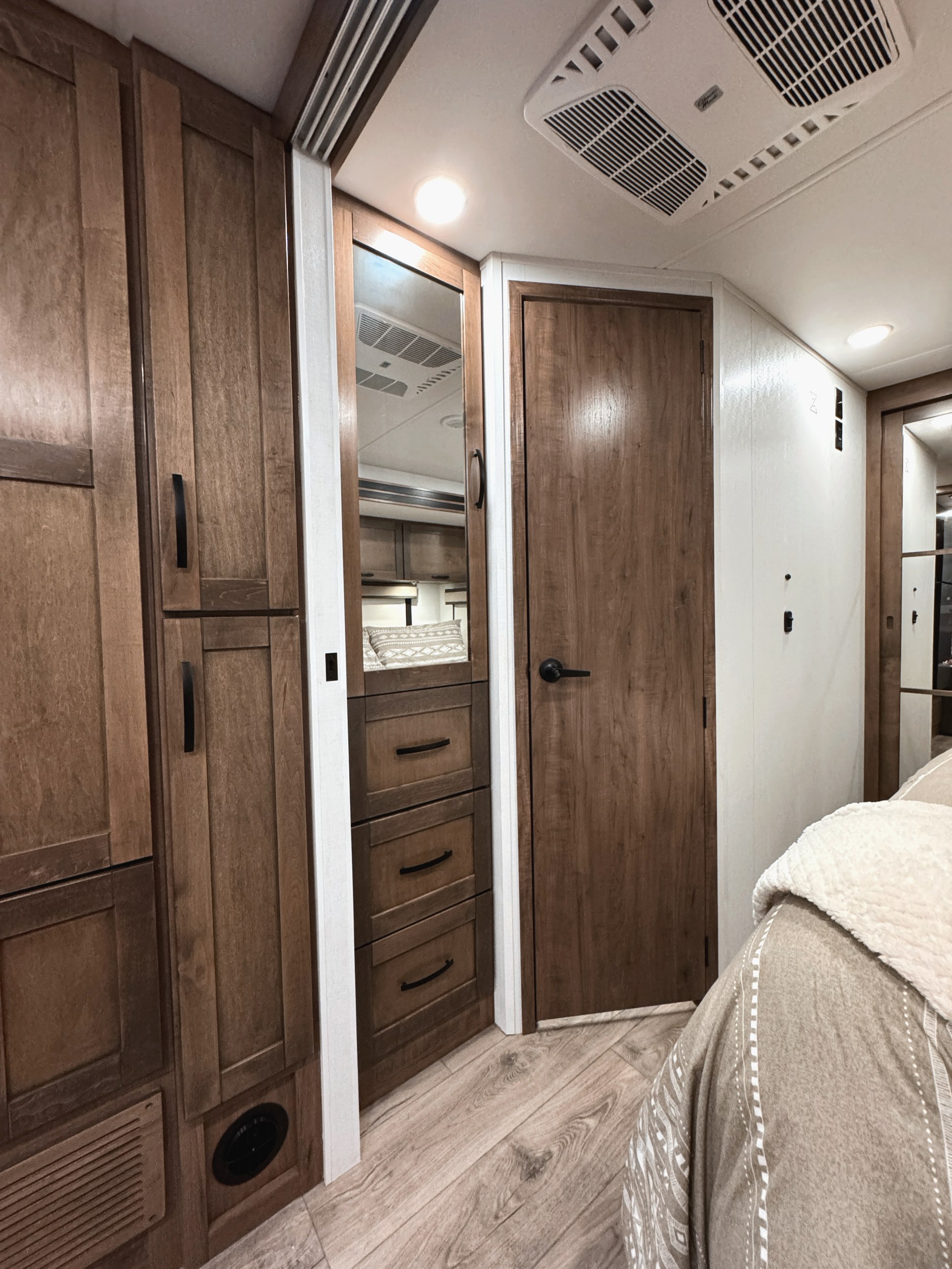 Modern RV rental interior with wood cabinets, mirror, ceiling AC, and cozy bedding. Ample storage in this travel-ready bedroom.. Jayco Greyhawk XL 32U 2026