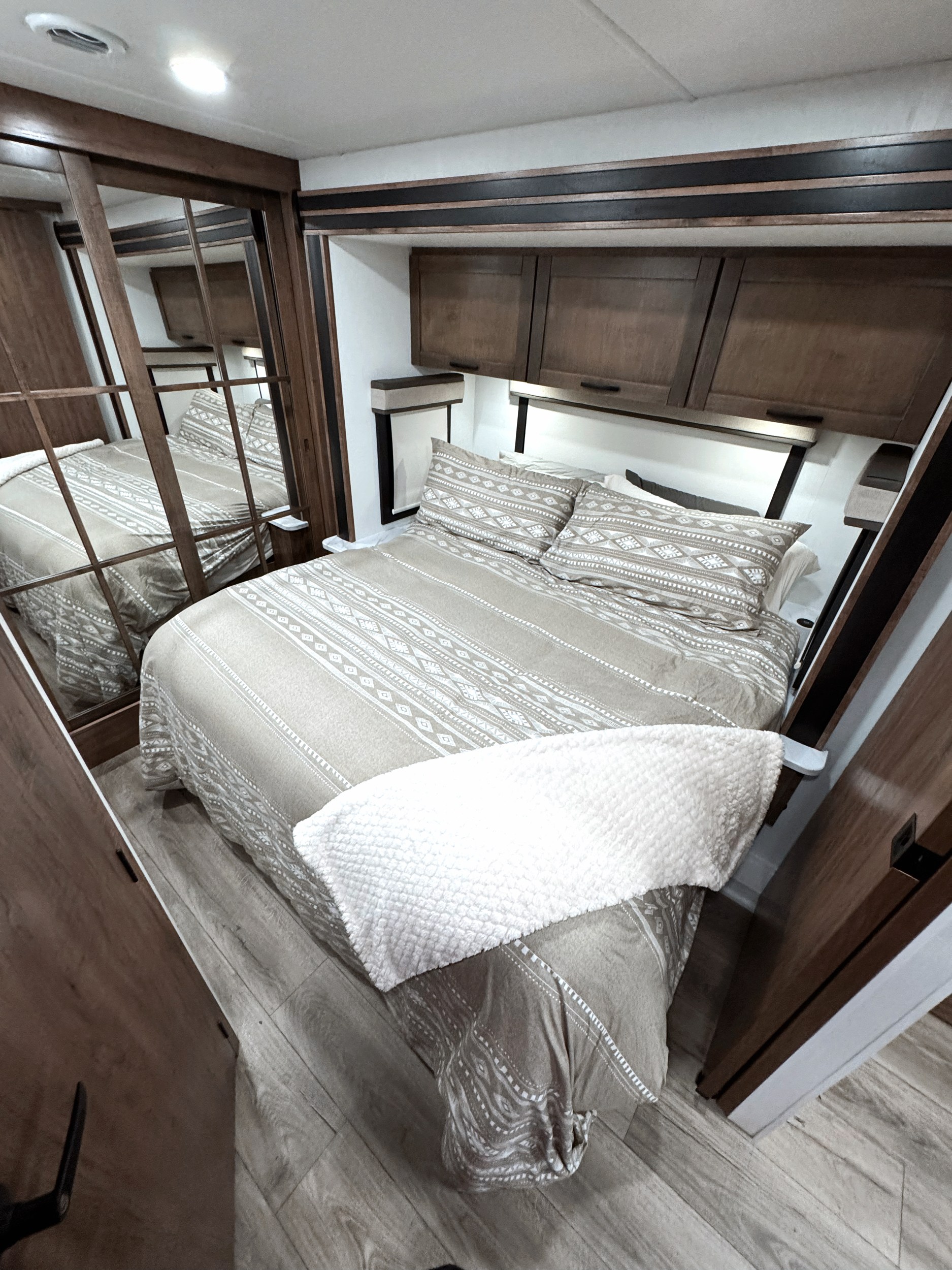 This RV rental's cozy bedroom features a patterned bedspread, overhead storage, and mirrored closet. A comfortable interior.. Jayco Greyhawk XL 32U 2026