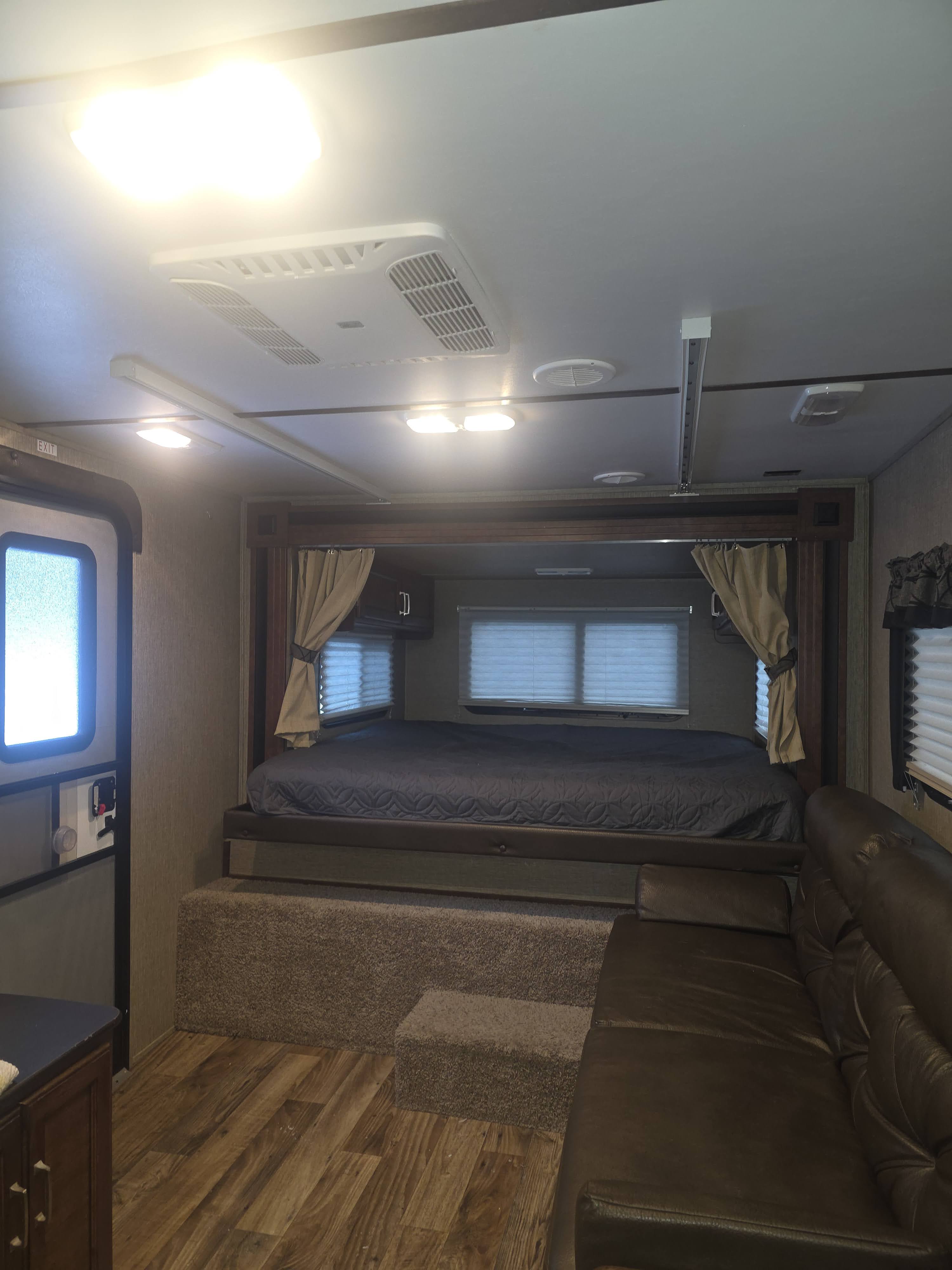 Inside an RV rental: a raised bed with privacy curtains, a plush leather sofa, and modern ceiling lights create a cozy interior.. Keystone RV Outback Ultra-Lite 2017