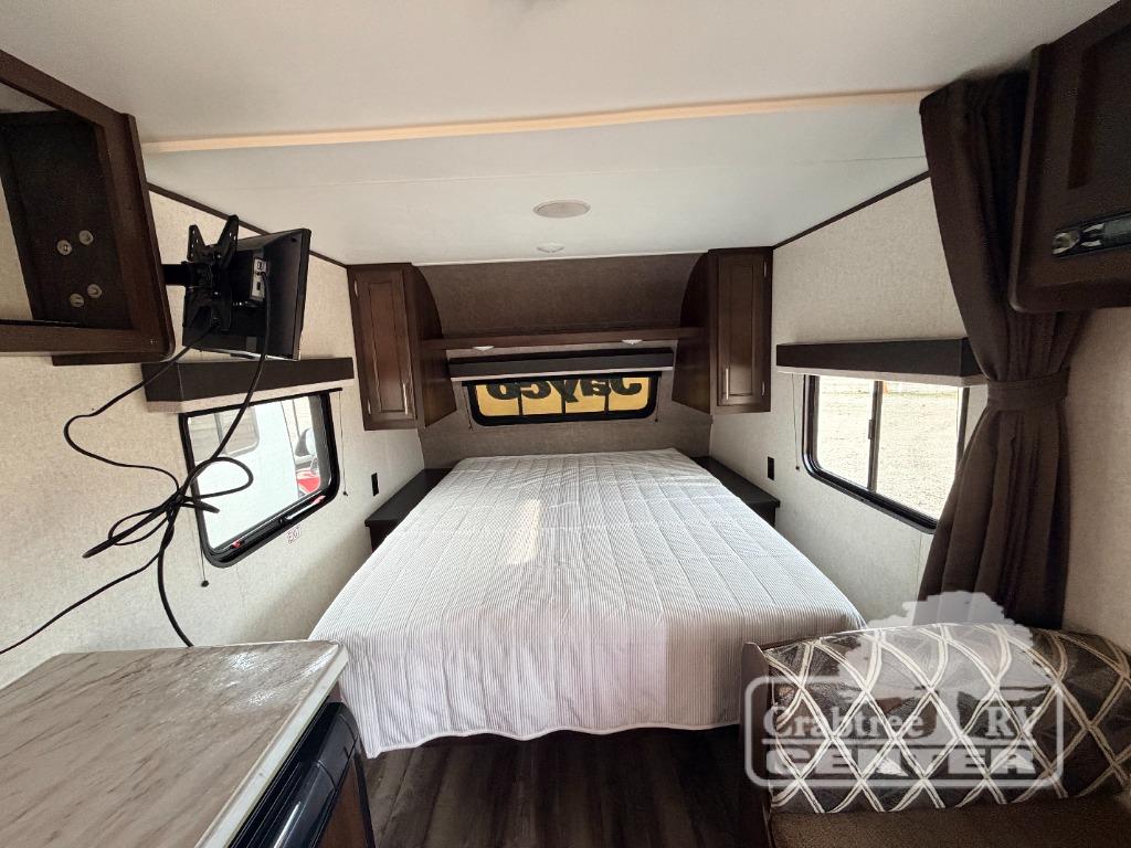 Explore this RV rental's cozy bedroom, offering a comfortable bed, mounted TV, overhead storage, and side windows.. Jayco Jay Flight SLX 2019