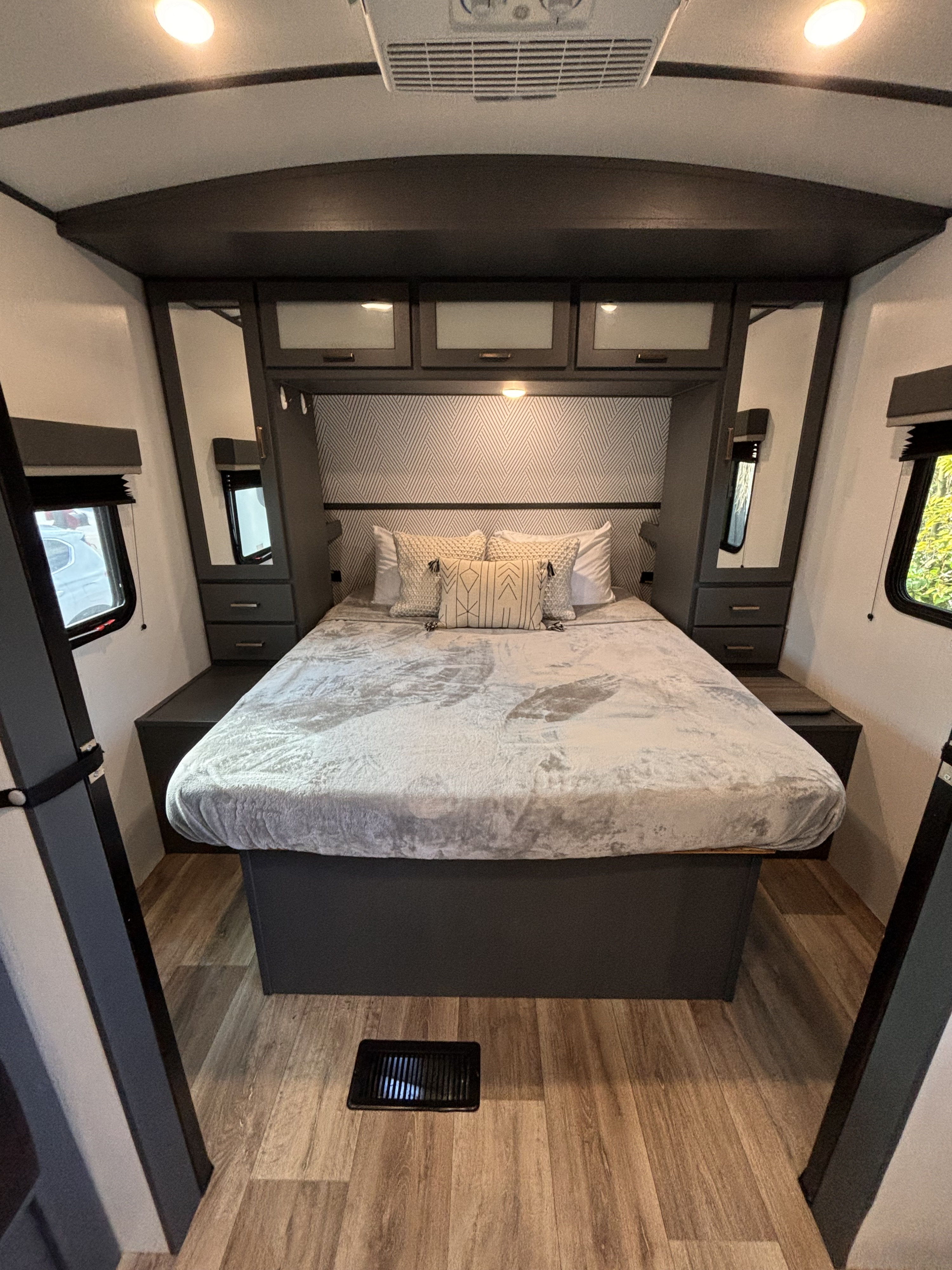 Modern RV rental bedroom featuring a large bed, ample overhead storage, built-in side tables, and natural light from windows.. Keystone RV Bullet 2022