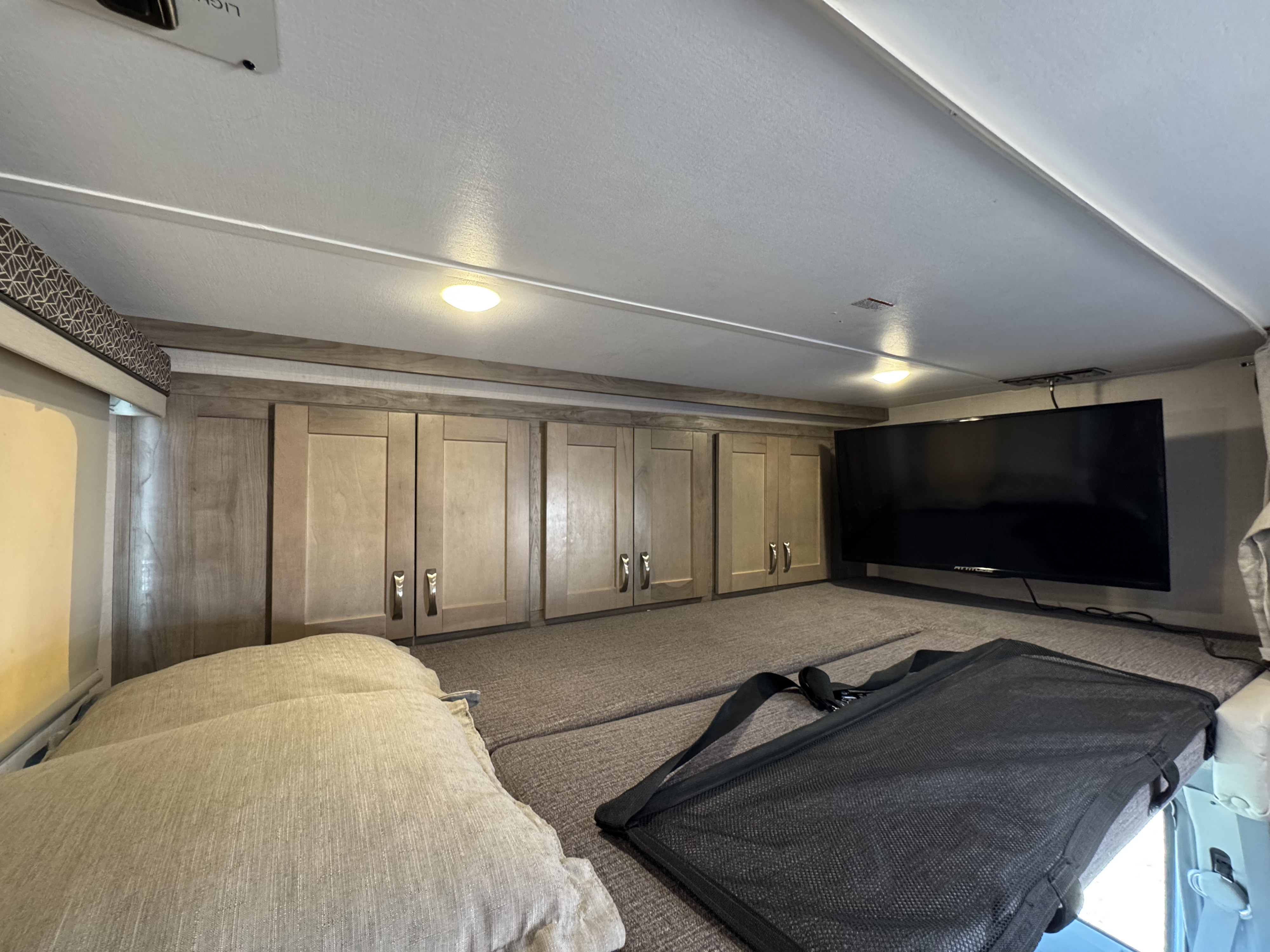 RV rental bunk area featuring overhead cabinets, a flat-screen TV, and a safety net for context.. Gulf Stream 63111 2024
