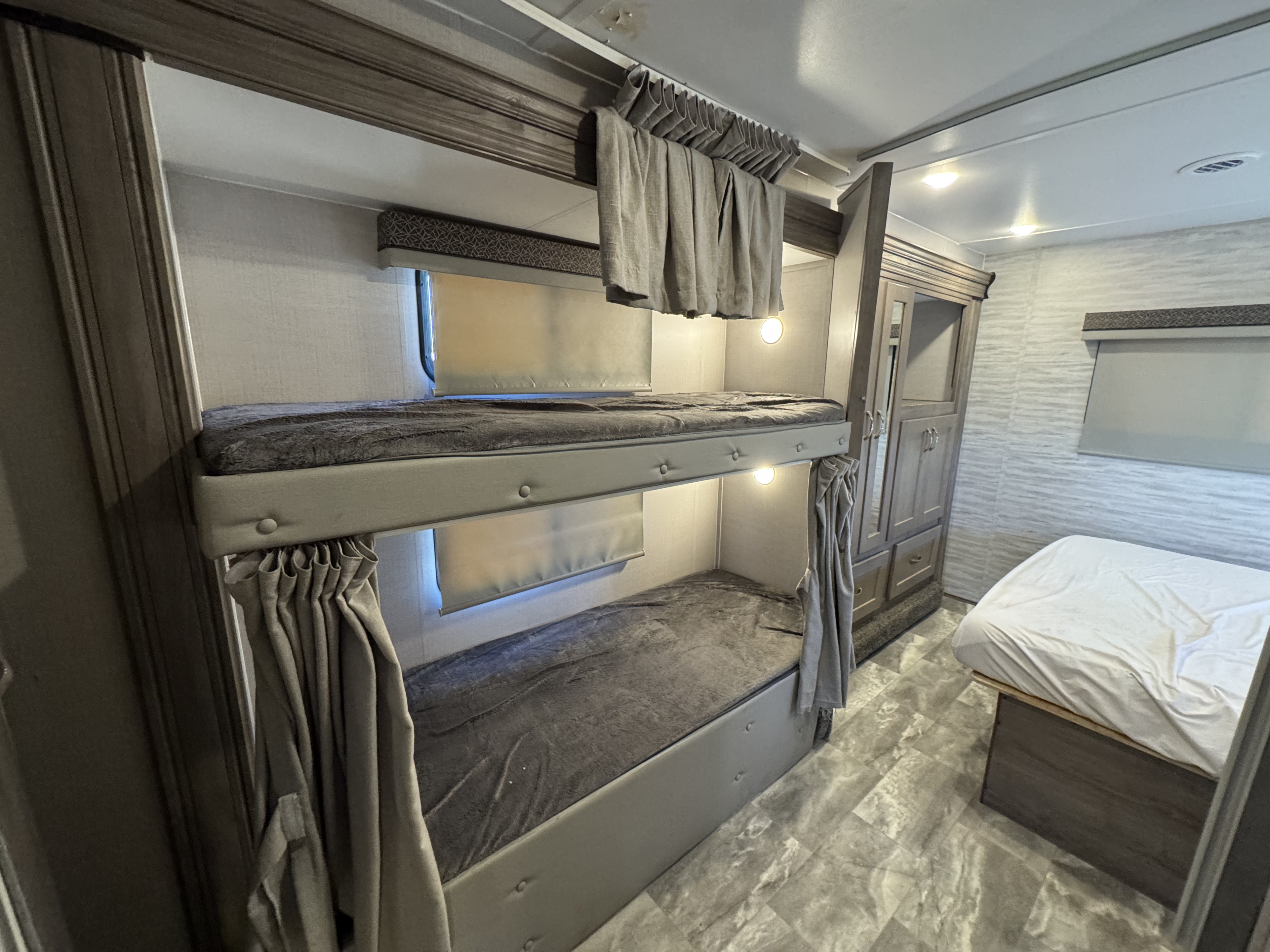 RV rental bedroom view: plush bunk beds with curtains & lights, plus a main bed in a modern interior.. Gulf Stream 63111 2024
