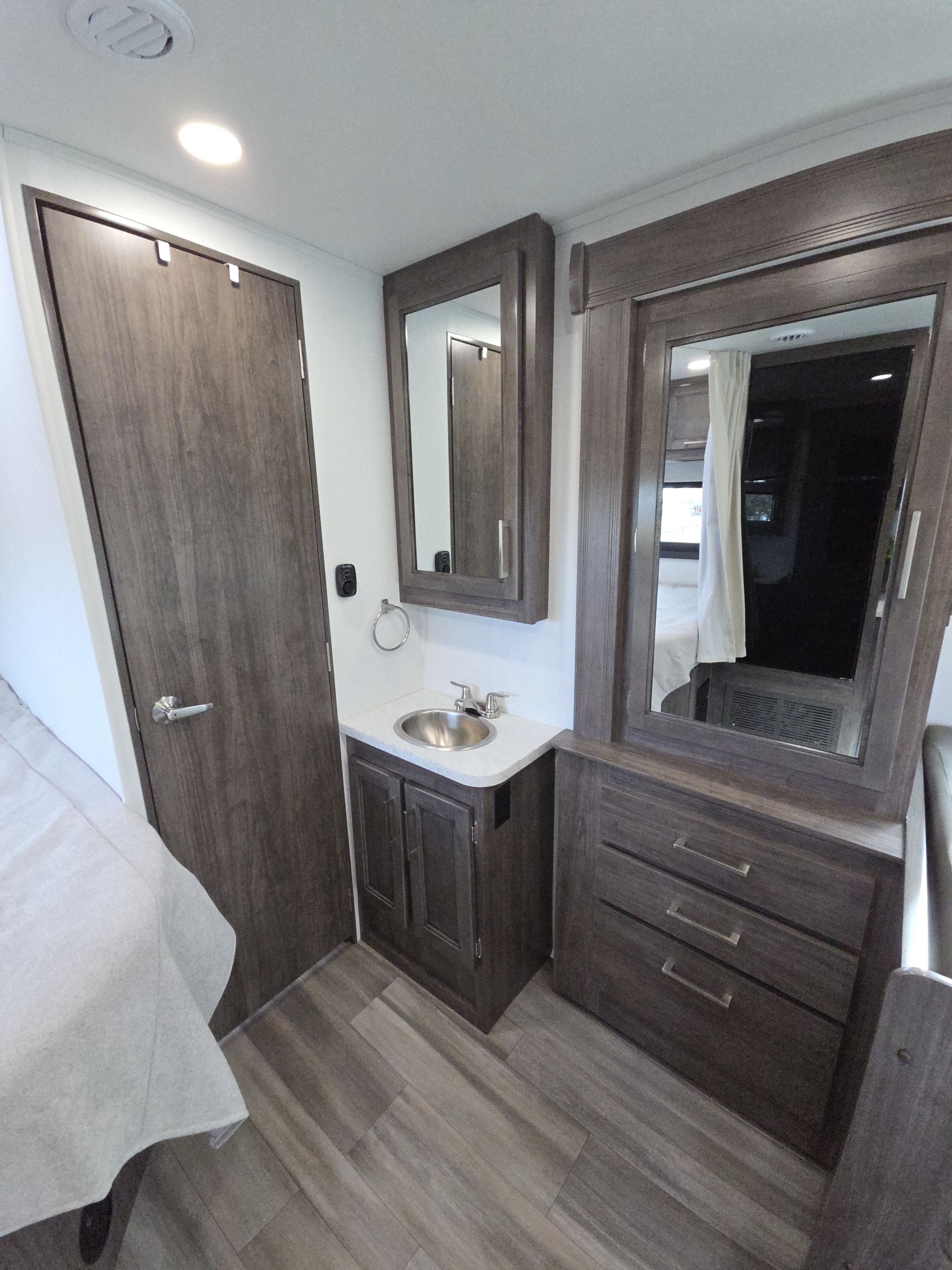 This RV rental features a modern bedroom area with a bathroom vanity, mirror, and dresser, offering comfort and storage.. Jayco Redhawk SE 2026