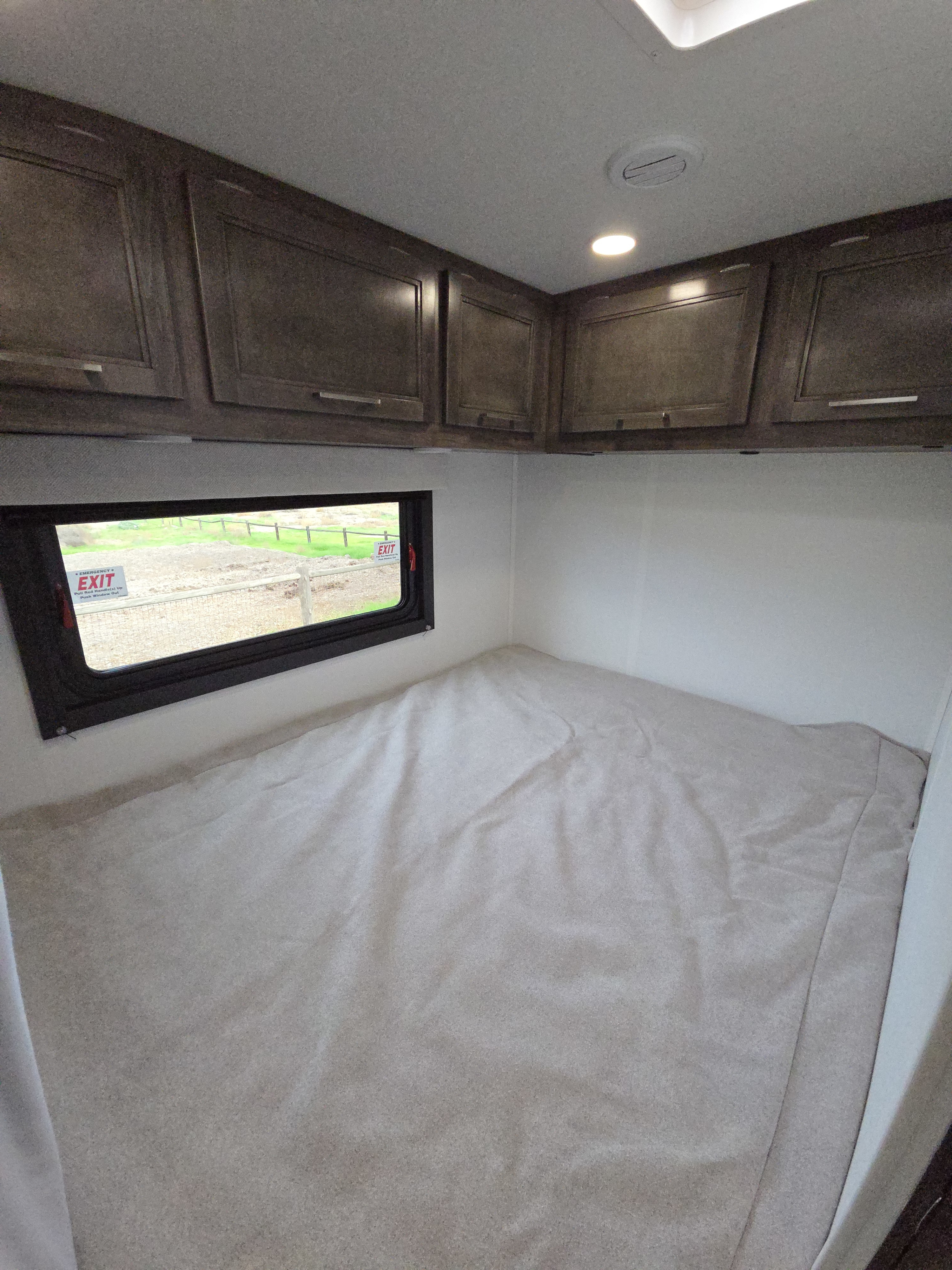 This RV rental's bedroom offers a comfortable bed, window with emergency exit sign, and convenient overhead cabinets.. Jayco Redhawk SE 2026