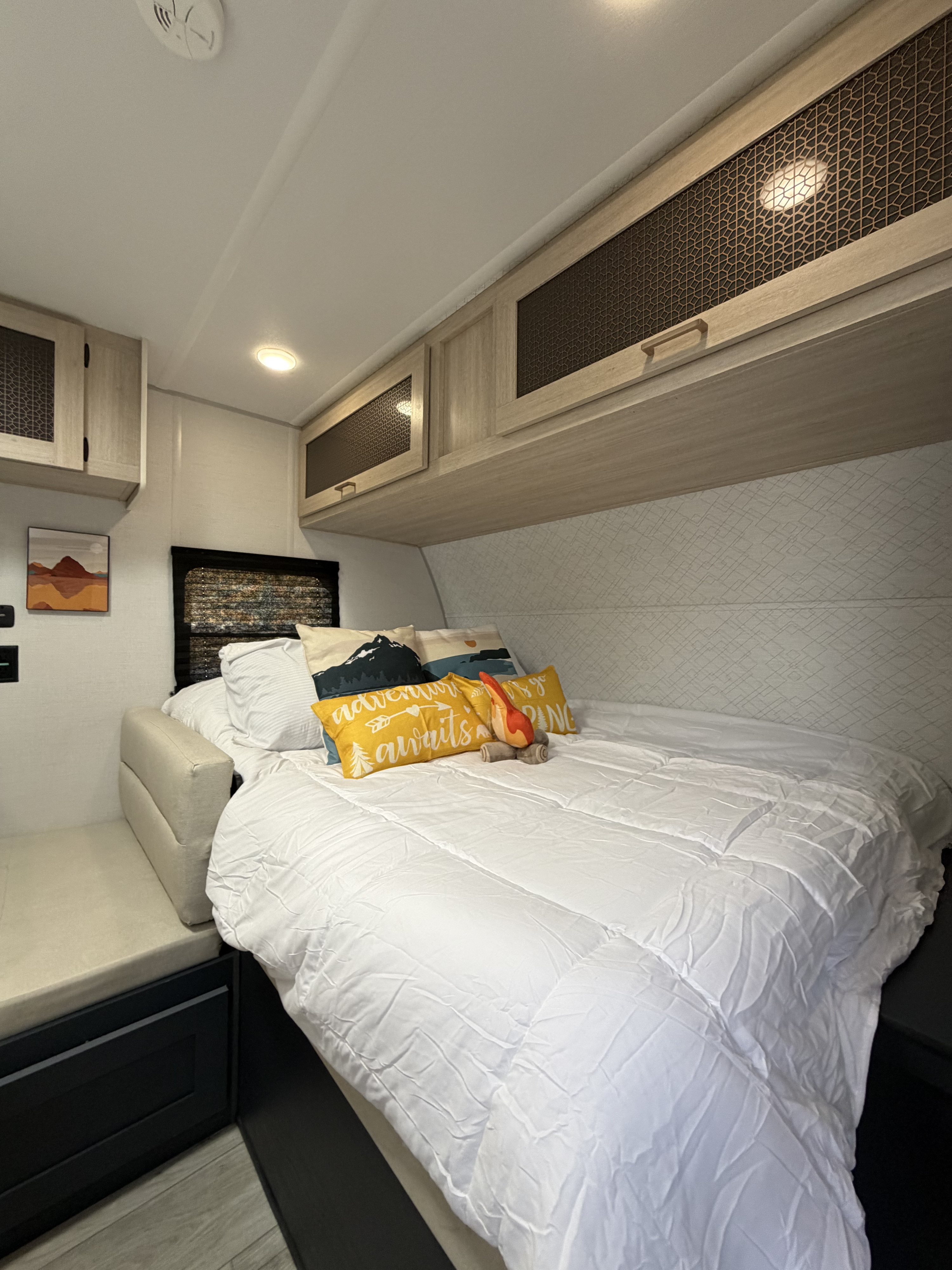 An inviting RV rental bedroom with a comfy bed, playful pillows, cabinets, and a side bench for relaxing.. Forest River Primetime Avenger 2025