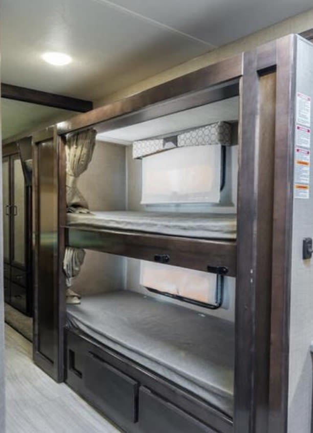 Inside an rv rental: dark wood bunk beds with mattresses, curtains, and small windows, offering a cozy sleeping area.. Thor Quantum SE 2020